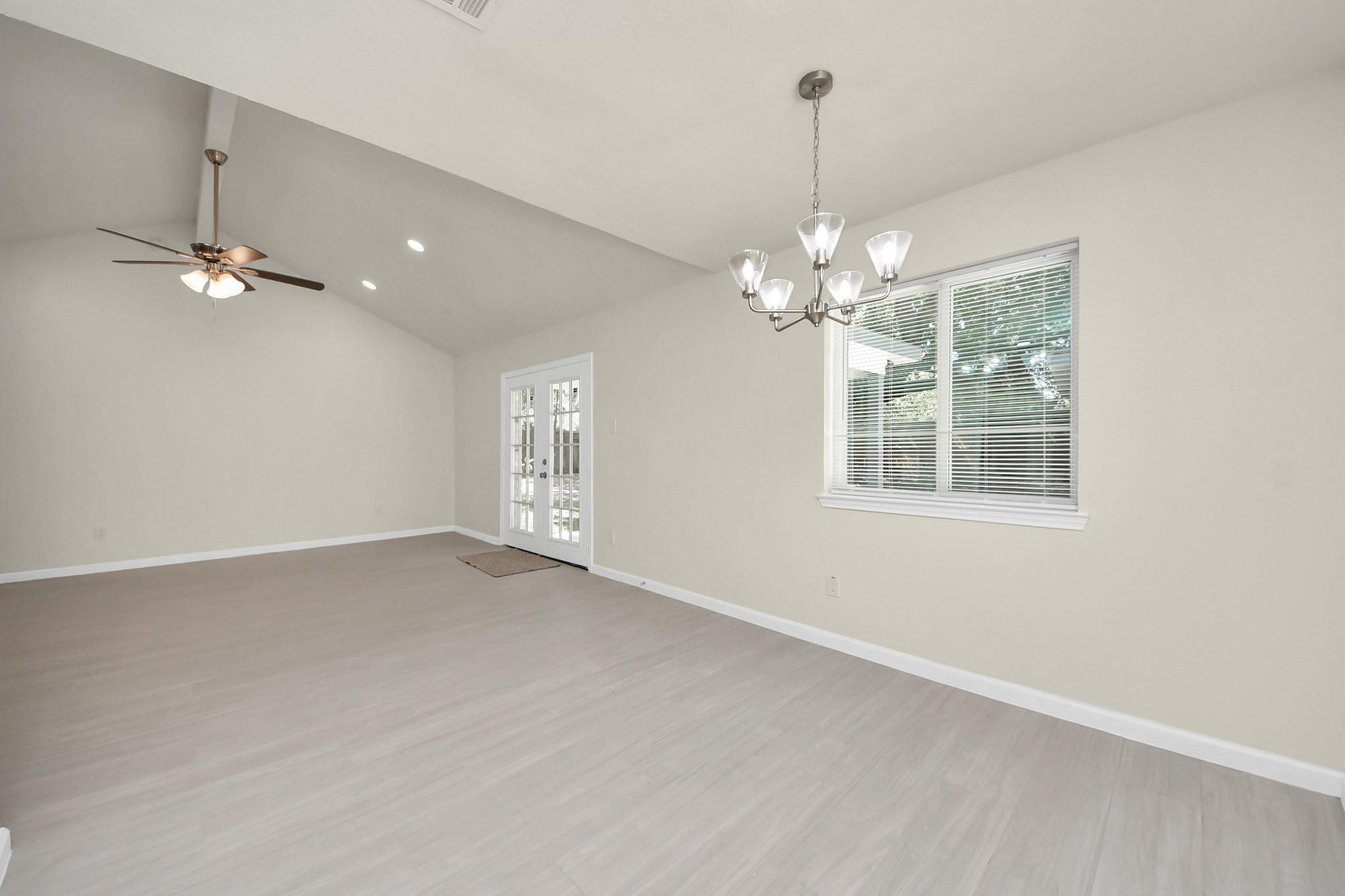 Empty living room with a high ceiling, ceiling fan, French doors, and a wide window with blinds.