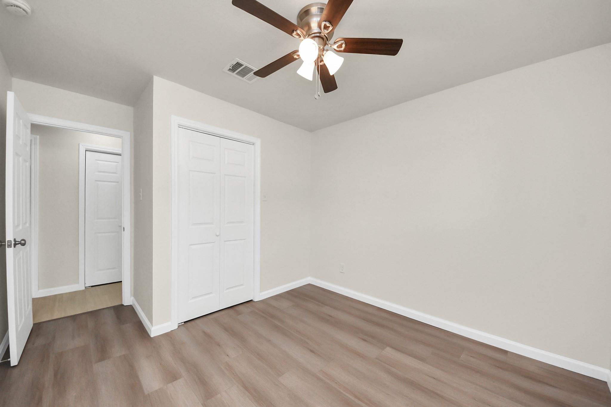 Vacant bedroom with wood-look flooring, double closet doors, and a ceiling fan with lights.