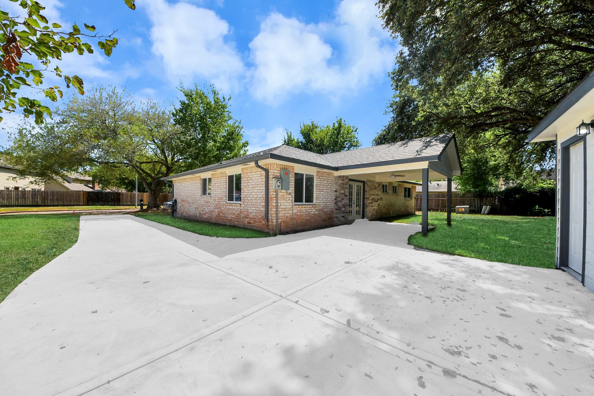 Brick house with a covered patio and broad concrete driveway beneath mature trees.