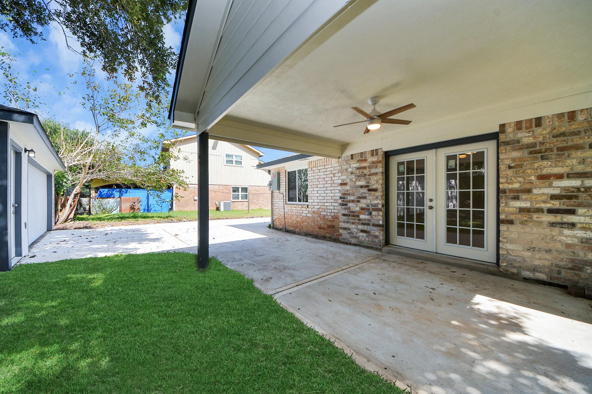 Covered backyard patio with brick walls, French doors, and a ceiling fan.
