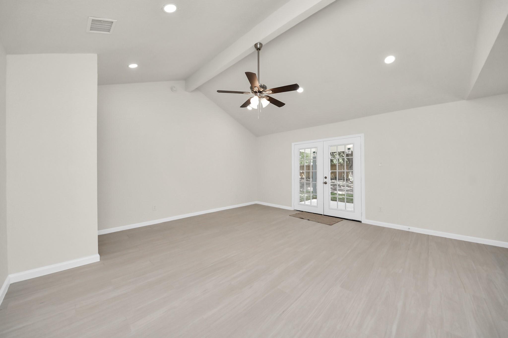 Empty room with vaulted ceiling, ceiling fan, pale flooring, and French doors to the yard.