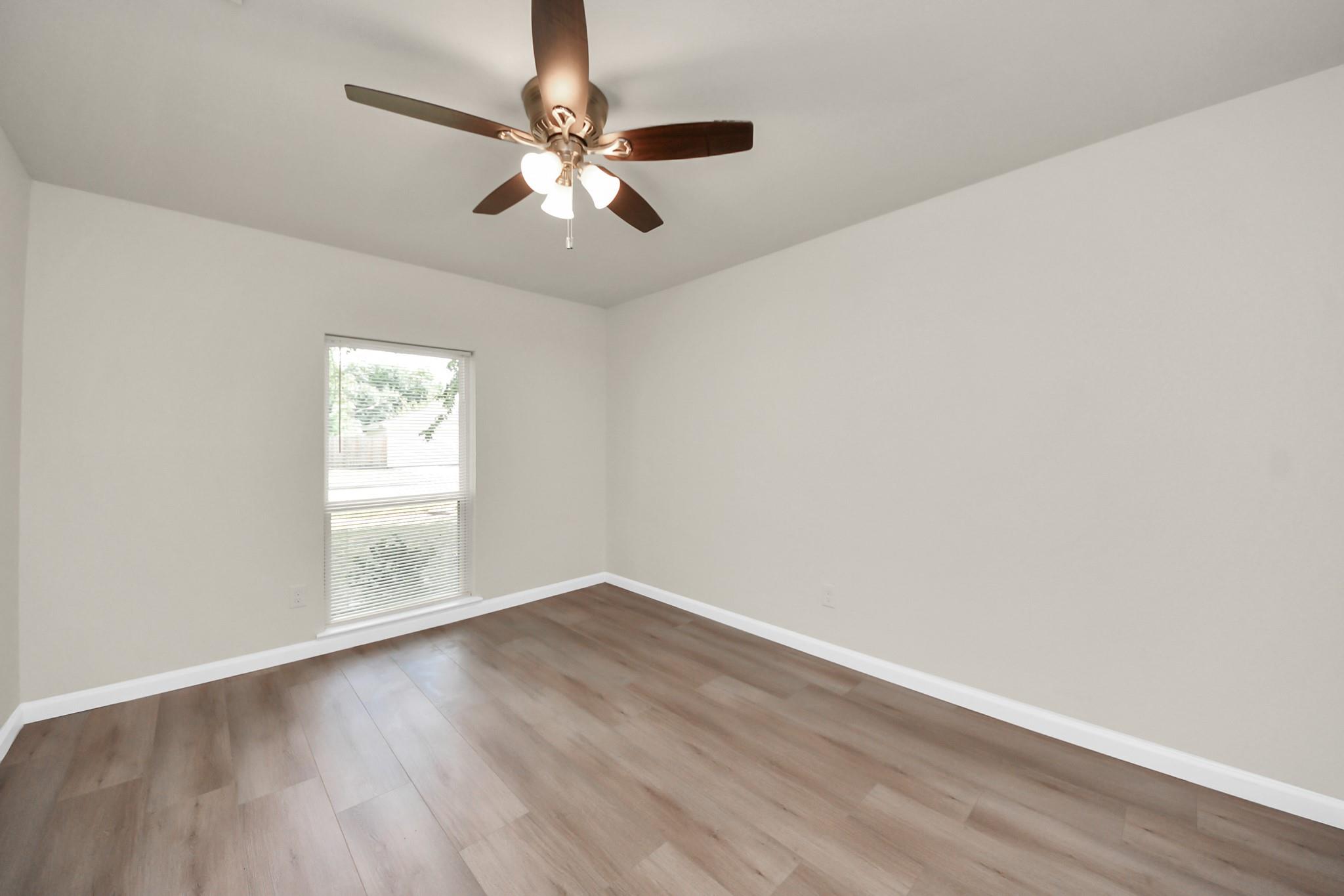 Empty bedroom with wood-look flooring, a window with blinds, and a ceiling fan.