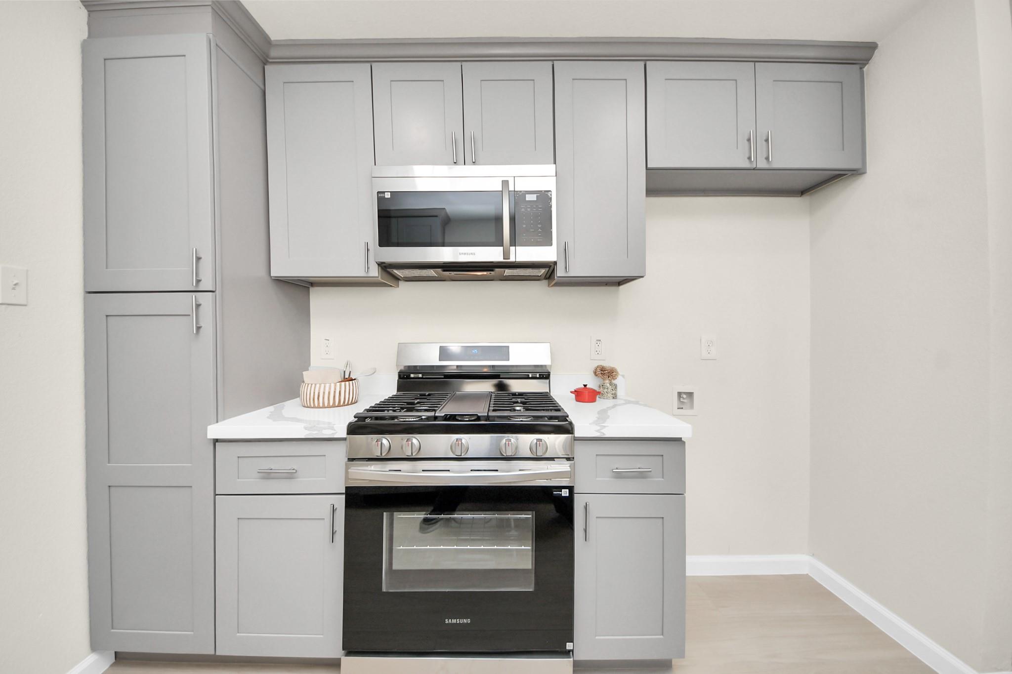 Kitchen with gray cabinets, white counters, and a stainless steel gas range beneath a microwave.