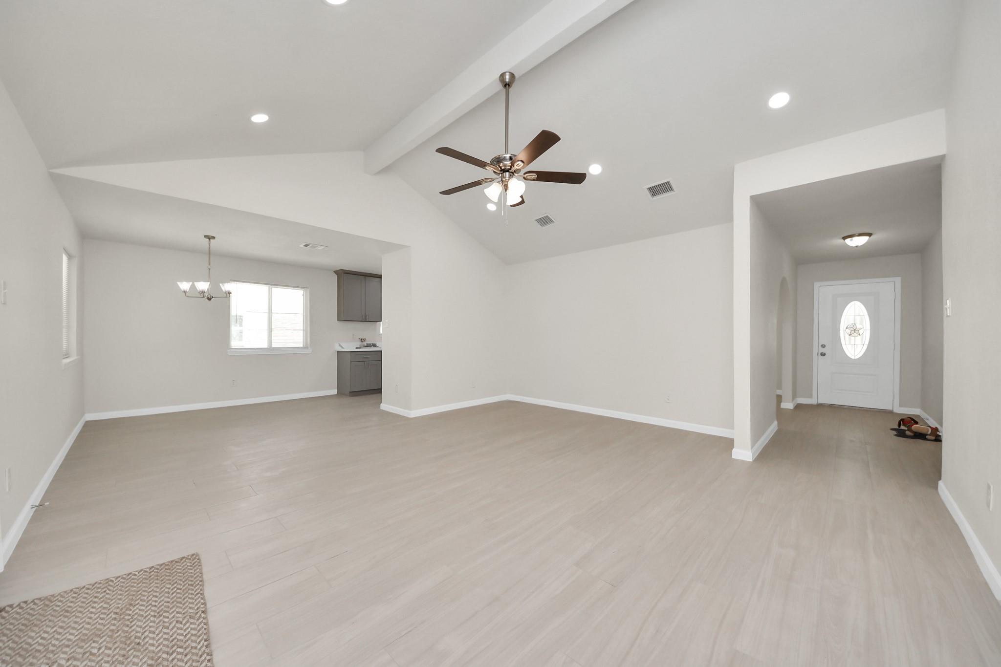 Open living and dining area with light flooring, vaulted ceiling, and ceiling fan.
