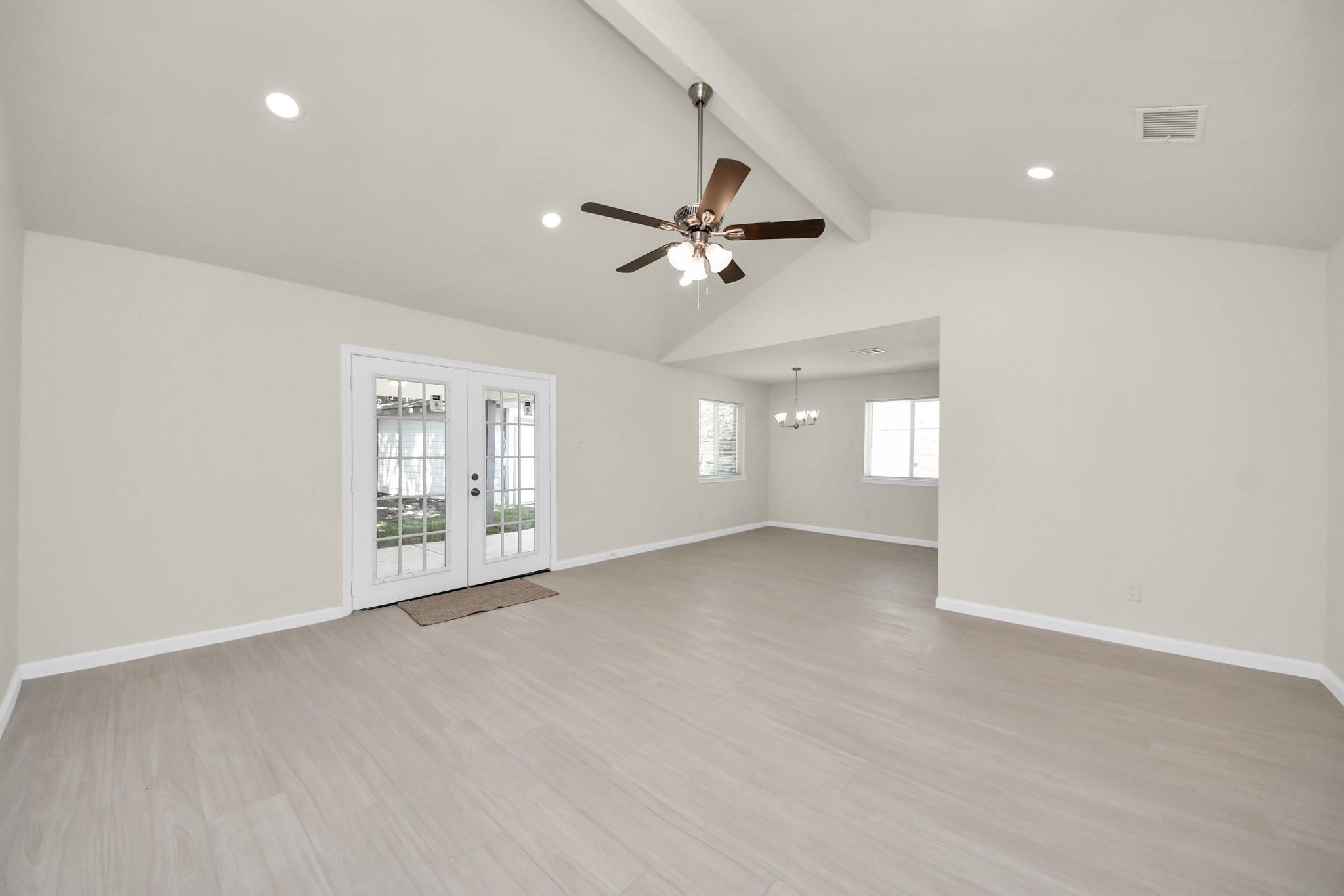 Empty living room with vaulted ceiling, light flooring, ceiling fan, and French doors to a patio.