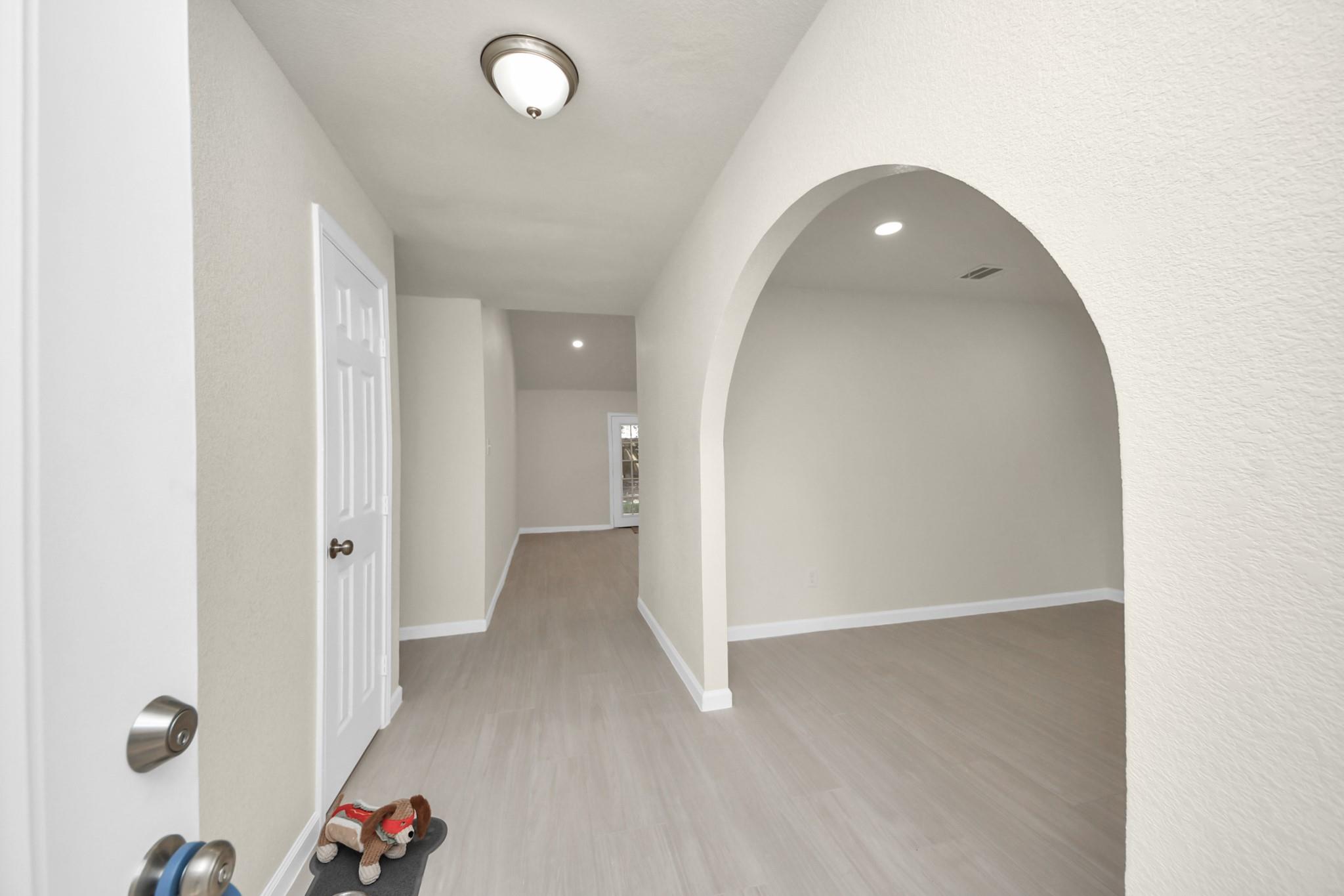 Hallway with gray flooring and a large arched opening into an adjoining room.