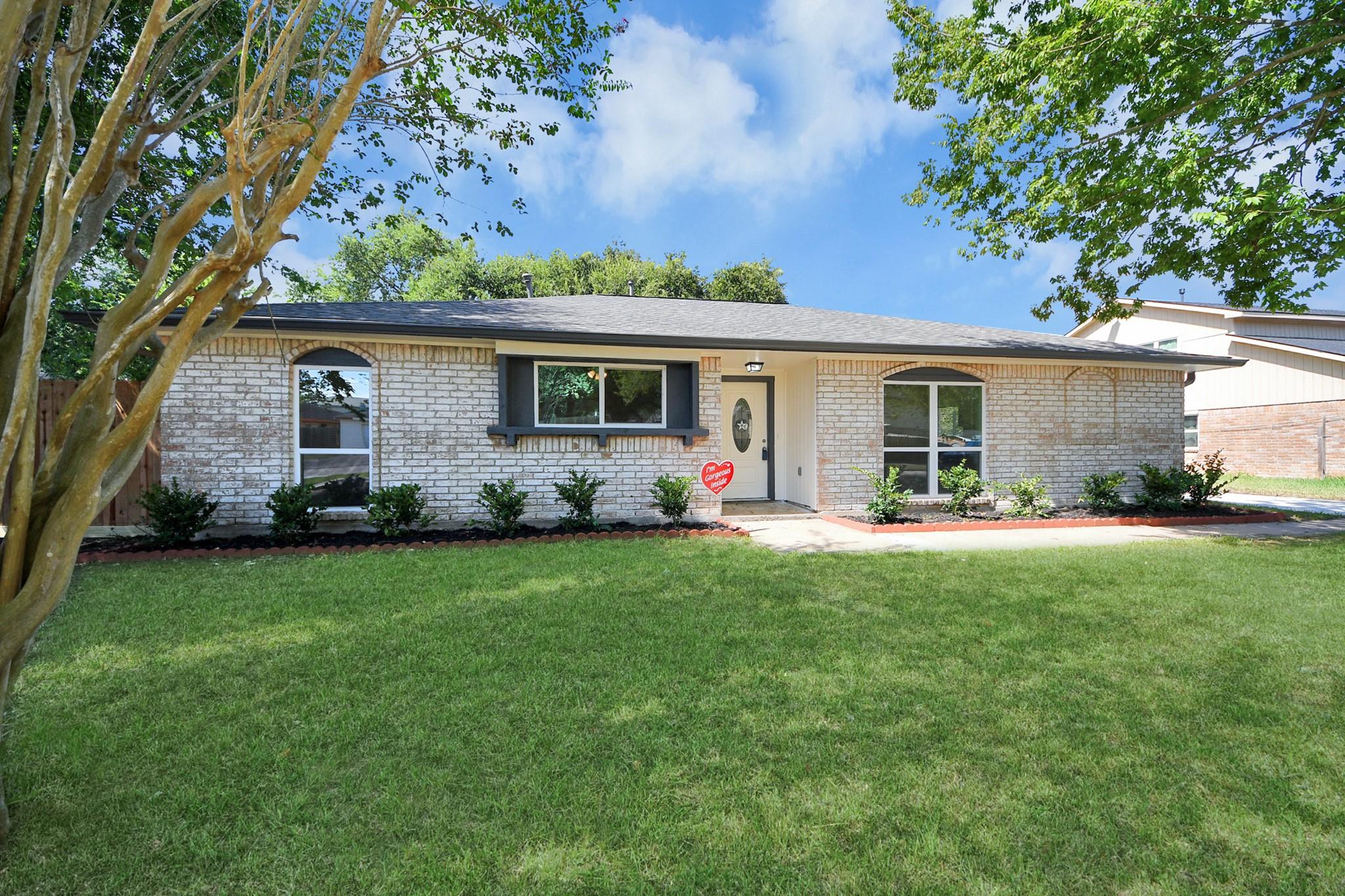 Single-story white brick house with arched windows, a broad lawn, and mature trees.