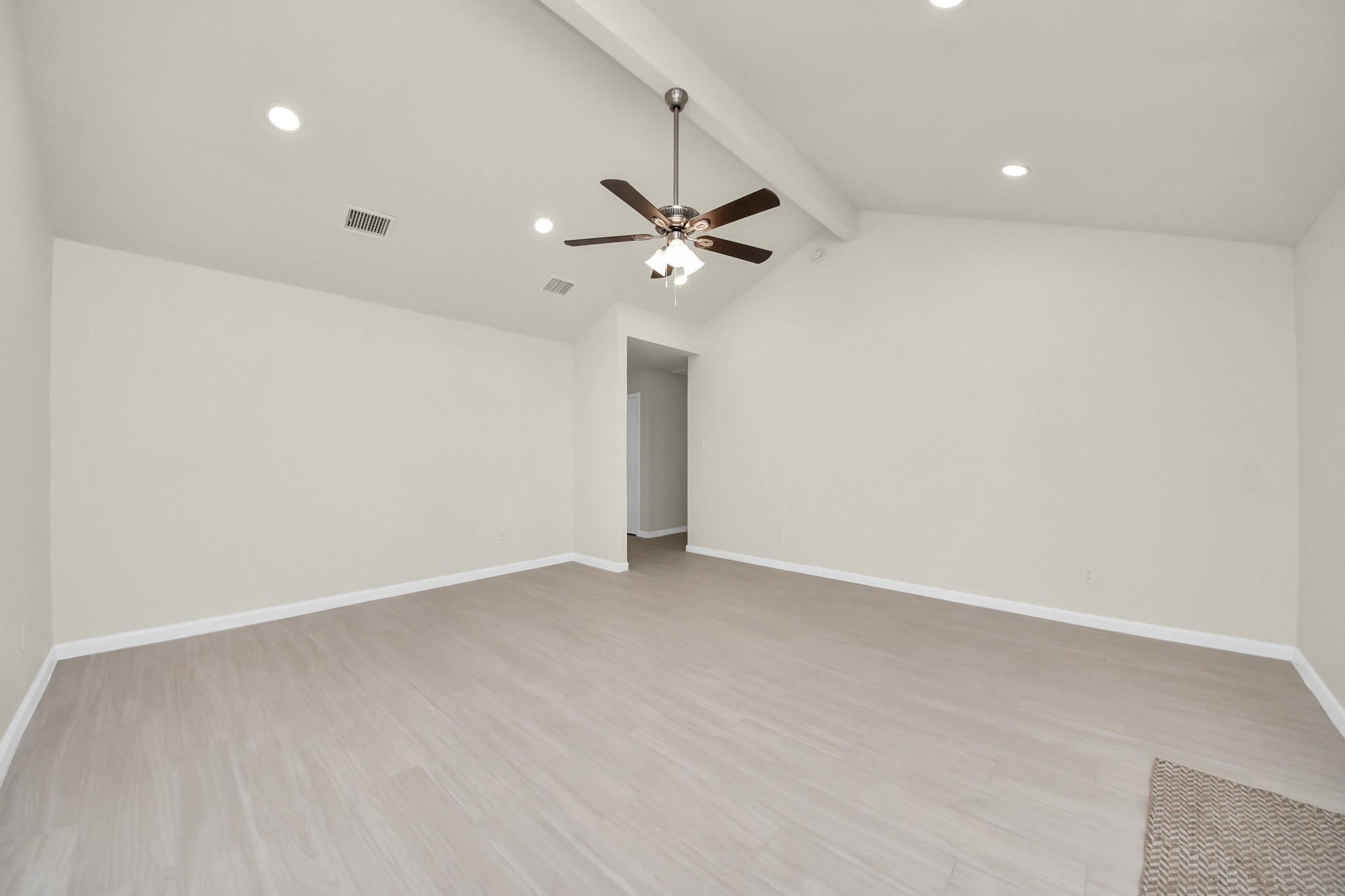 Empty room with vaulted ceiling, pale flooring, recessed lights, and a ceiling fan.