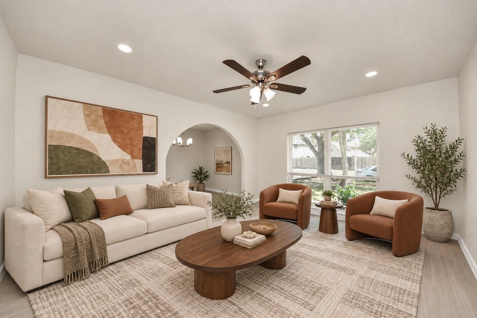 Staged living room with a cream sofa, rust-colored armchairs, an arched opening, and a large neutral rug.