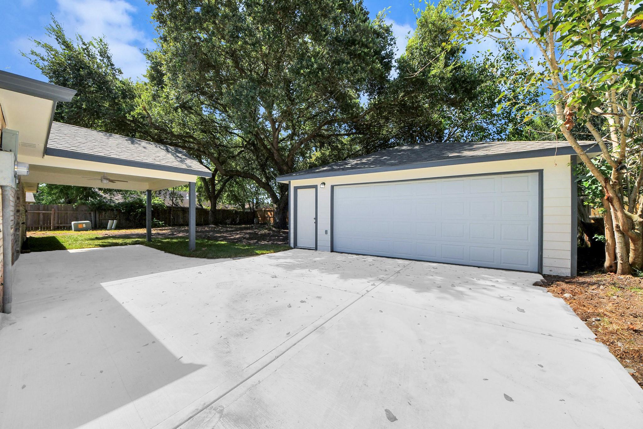 Detached white garage with double door beside a covered carport and broad concrete driveway.
