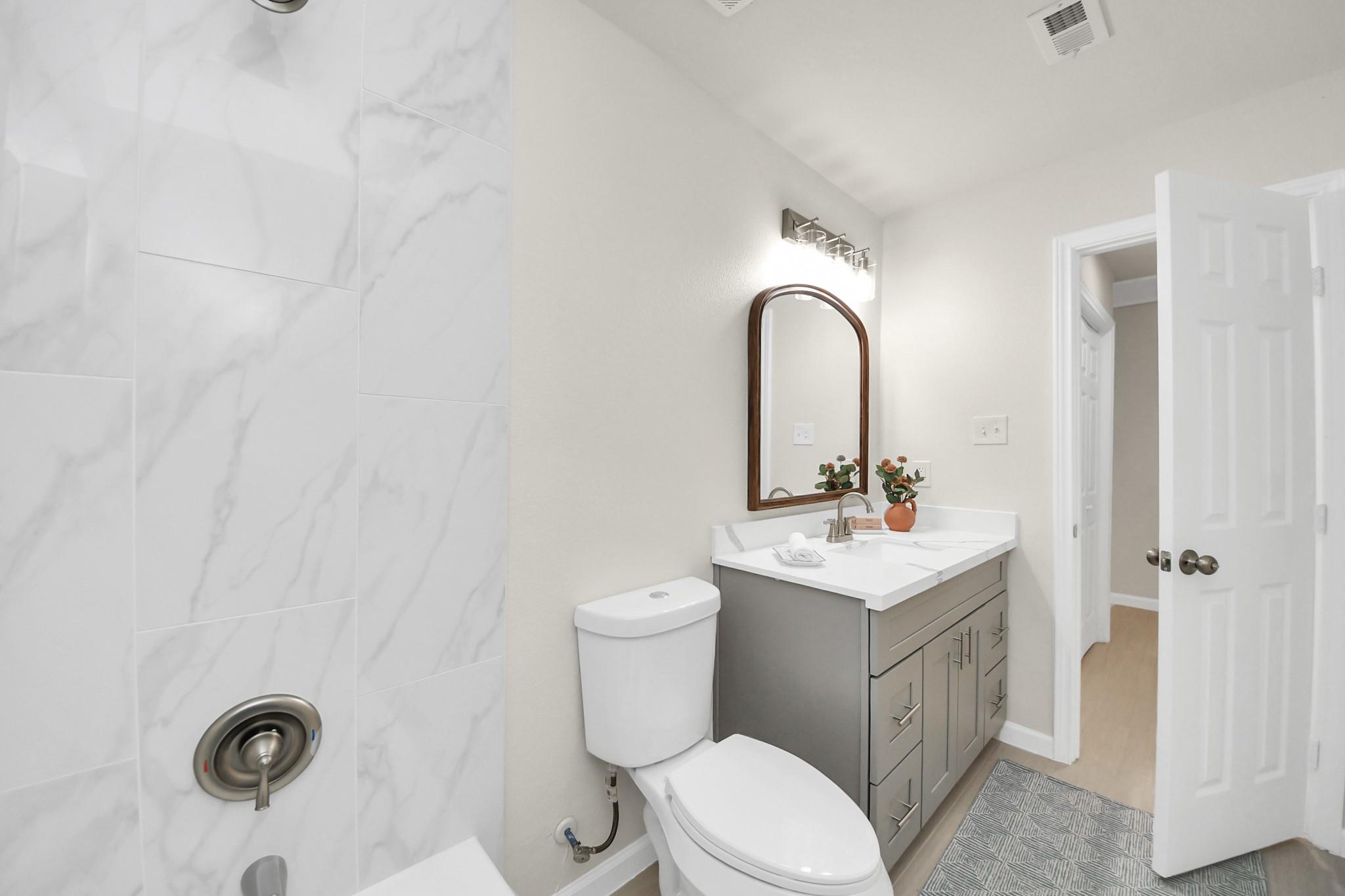 Bathroom with marble-look shower tile, gray vanity, and arched wood-framed mirror.