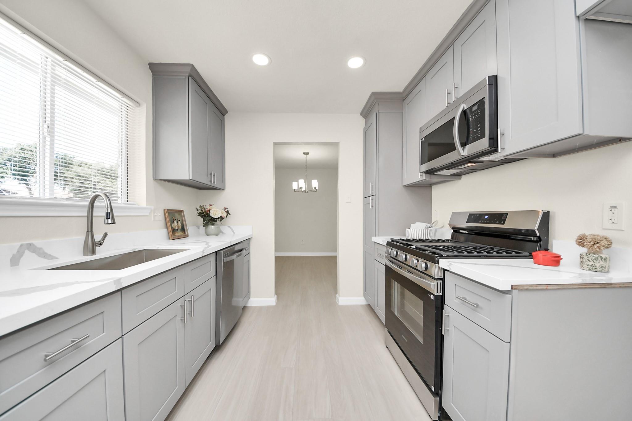 Bright kitchen with gray cabinets, white countertops, and stainless steel appliances.