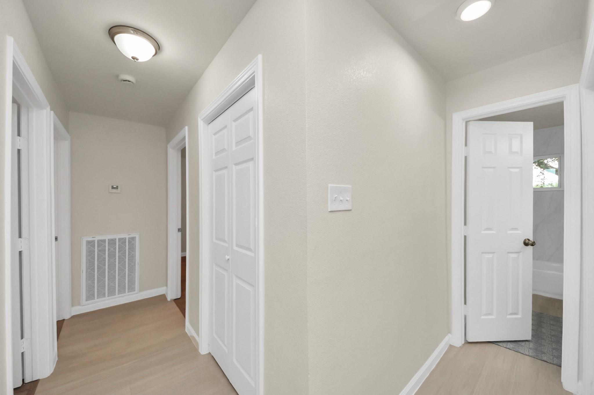 Hallway with light wood floors, white doors, and an open doorway to a bathroom.