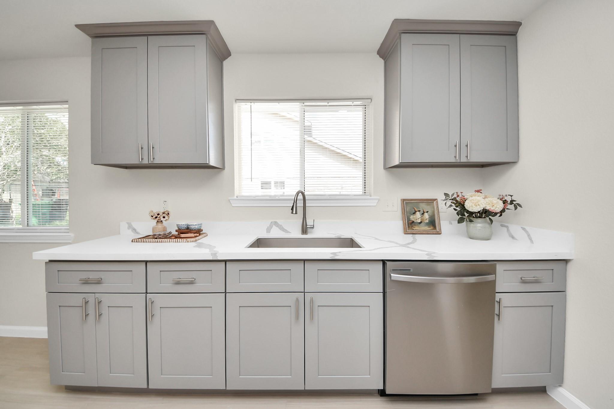 Kitchen with gray shaker cabinets, white counters, and a stainless steel dishwasher.