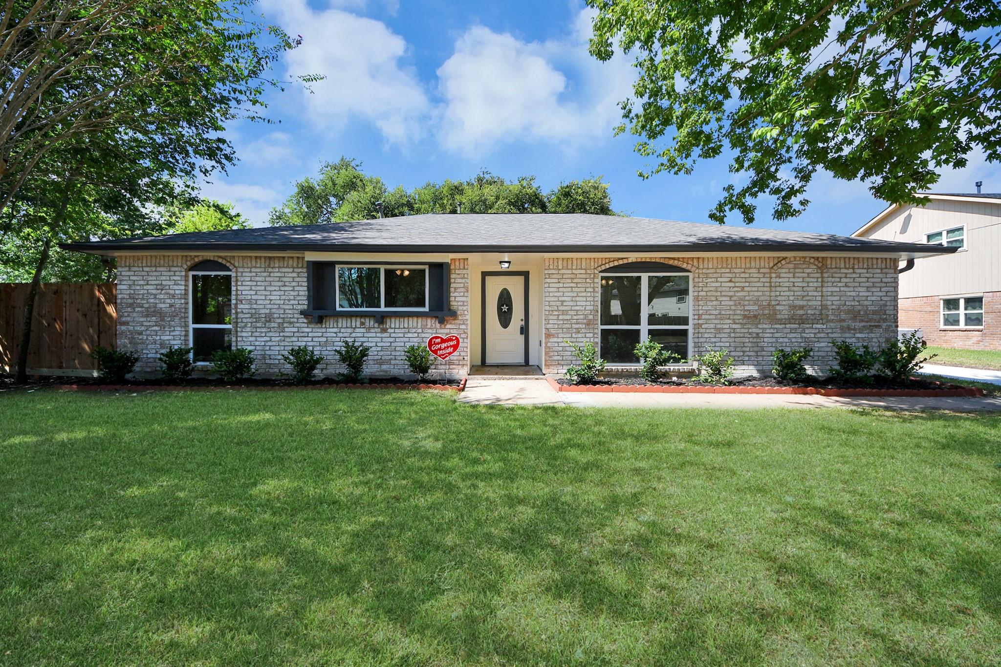 Single-story brick home with arched windows, a cream front door, and a broad green lawn.