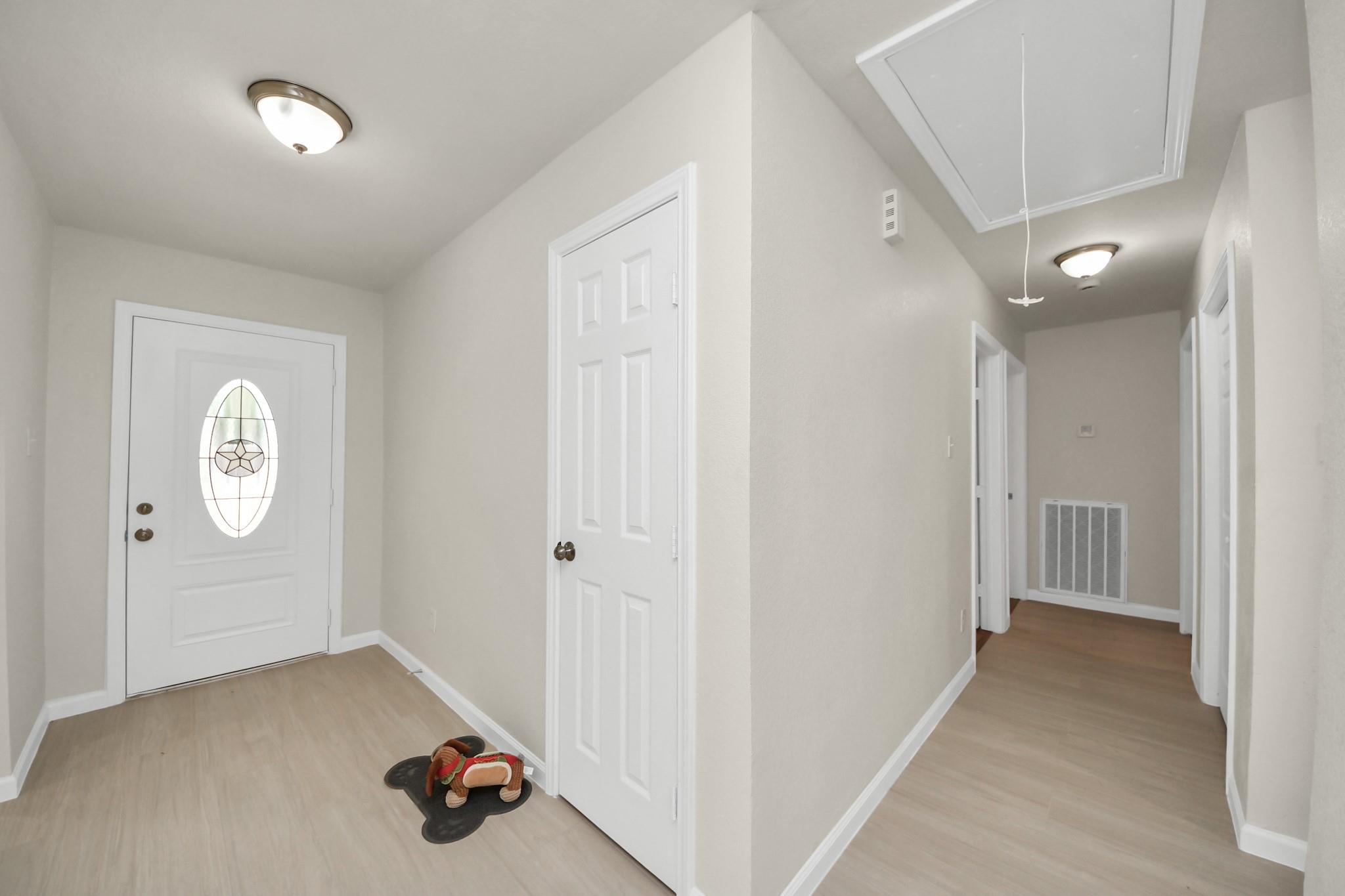 Entryway with an oval glass-panel front door and hallway beneath a ceiling attic access.