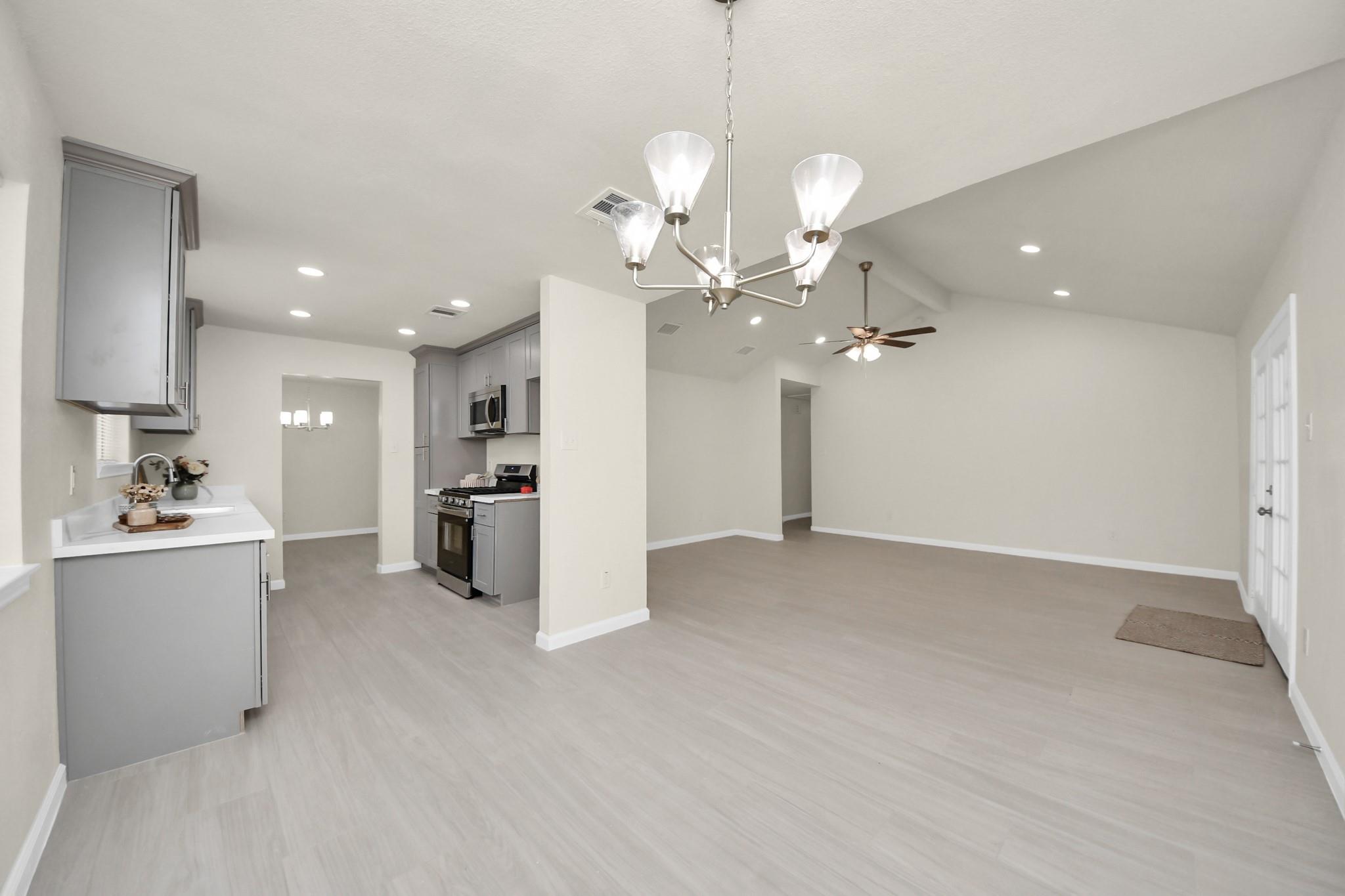 Open-plan kitchen and living area with gray cabinets, light flooring, vaulted ceiling, and chandelier.