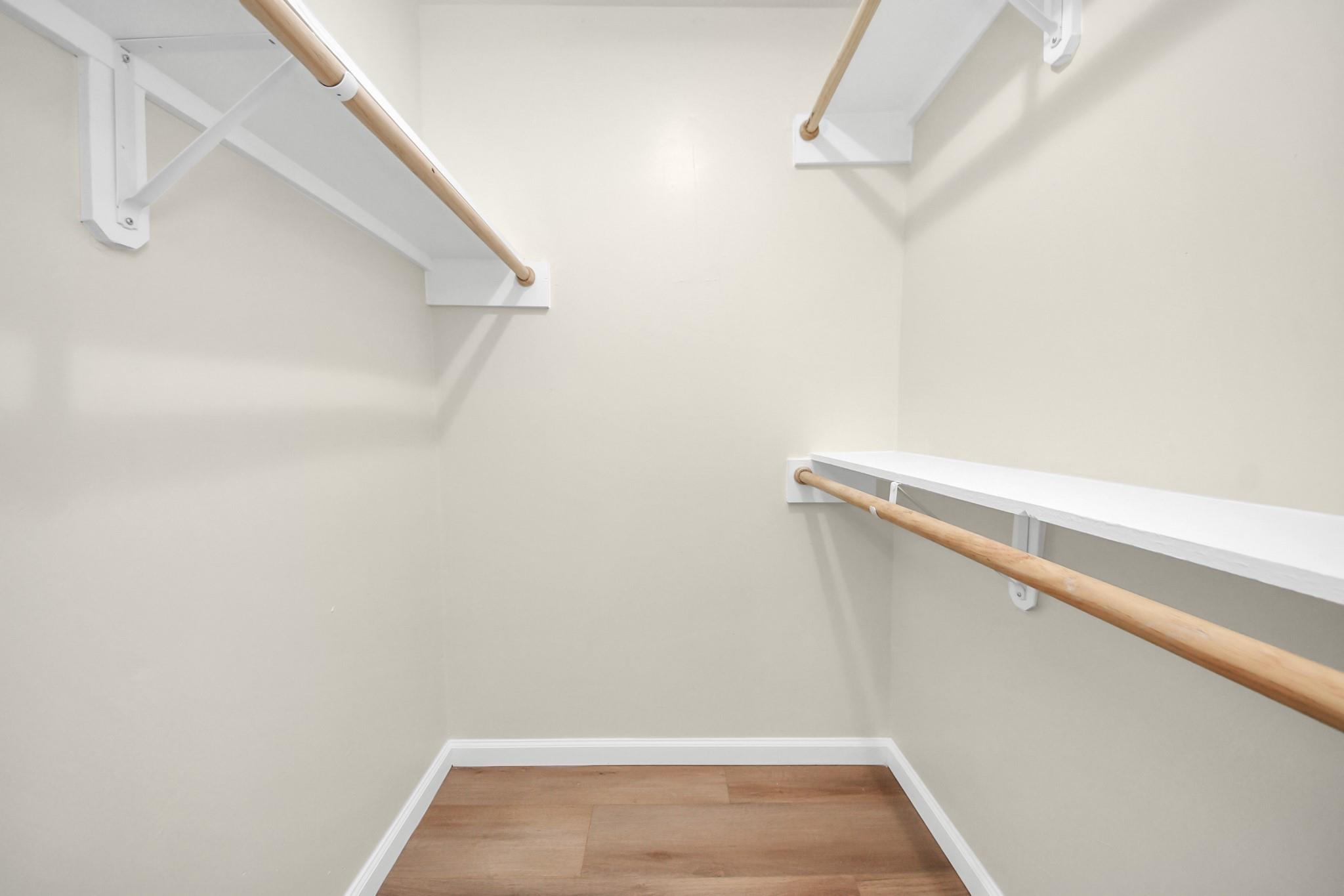 Empty walk-in closet with wooden hanging rods and wood-look flooring.