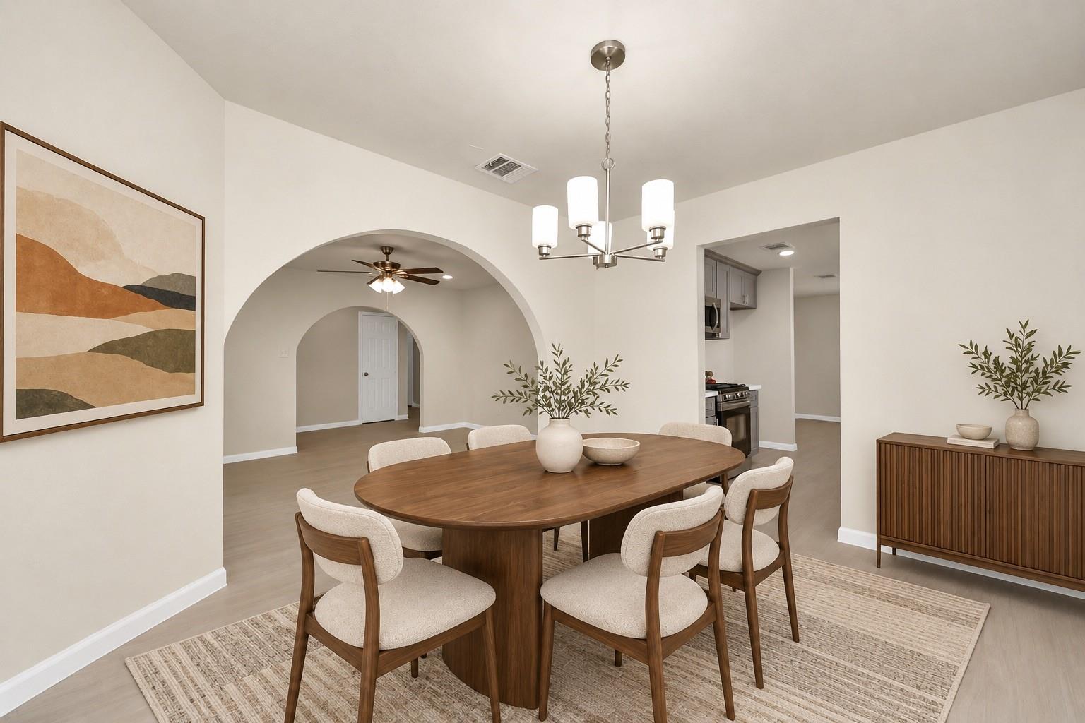 Dining room with a wood table, upholstered chairs, chandelier, and arched openings.