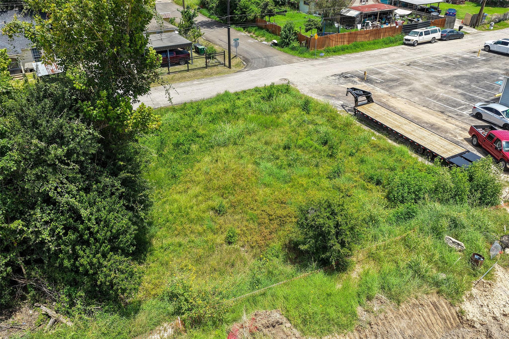 Aerial view of a grassy vacant lot bordered by trees beside a paved parking area.