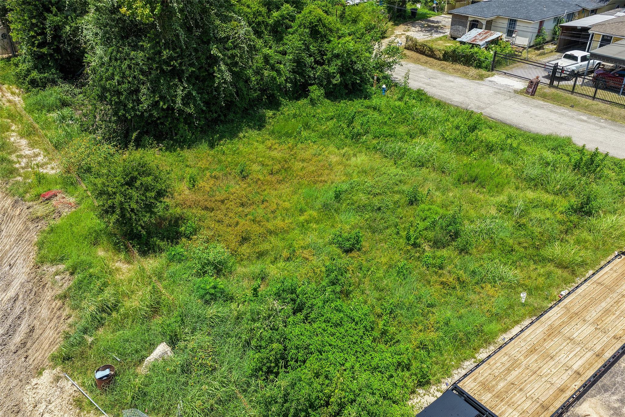 Aerial view of a vacant, overgrown lot beside a residential road and neighboring homes.