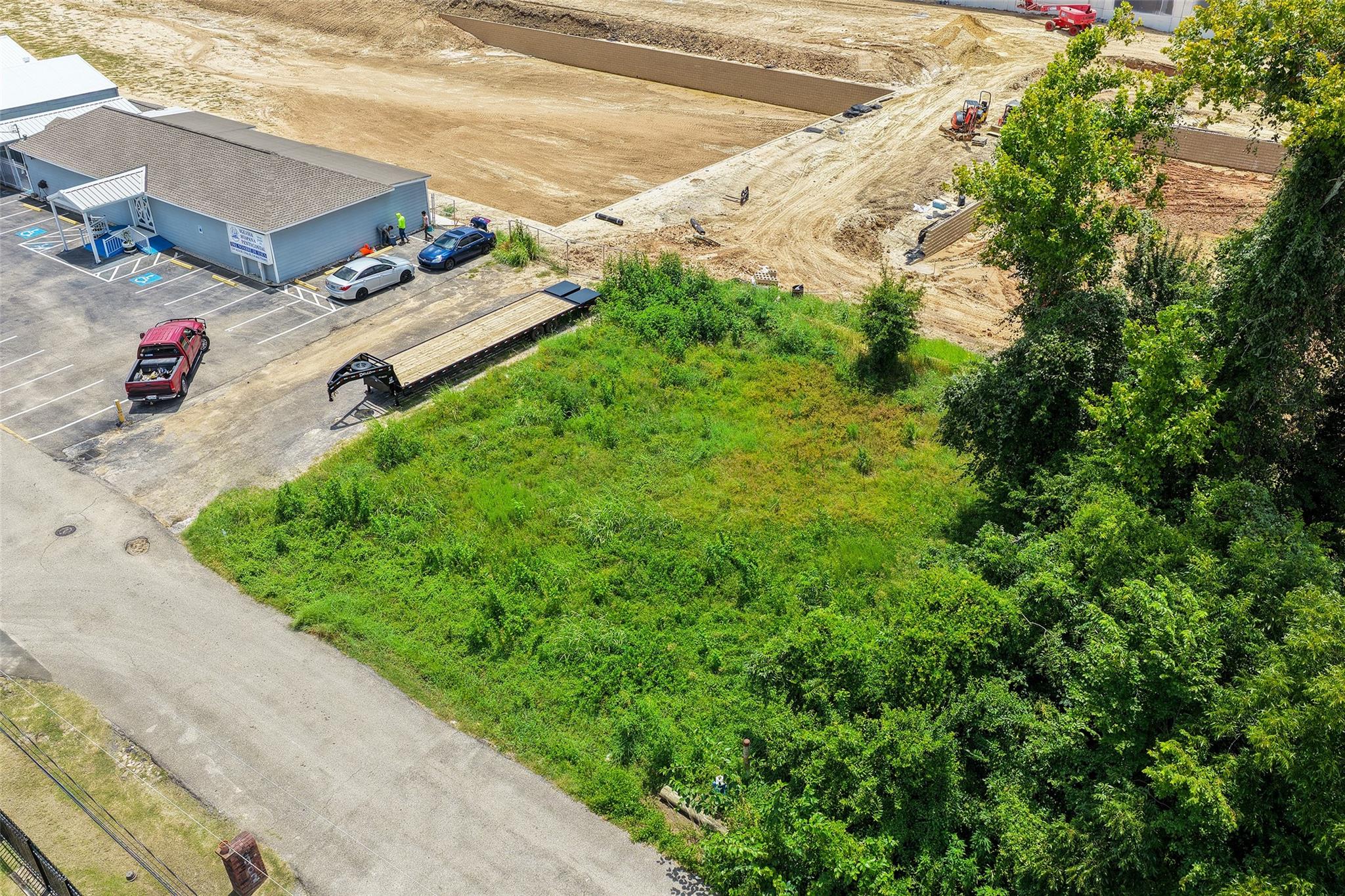Aerial view of a grassy vacant lot beside a parking area and active construction site.