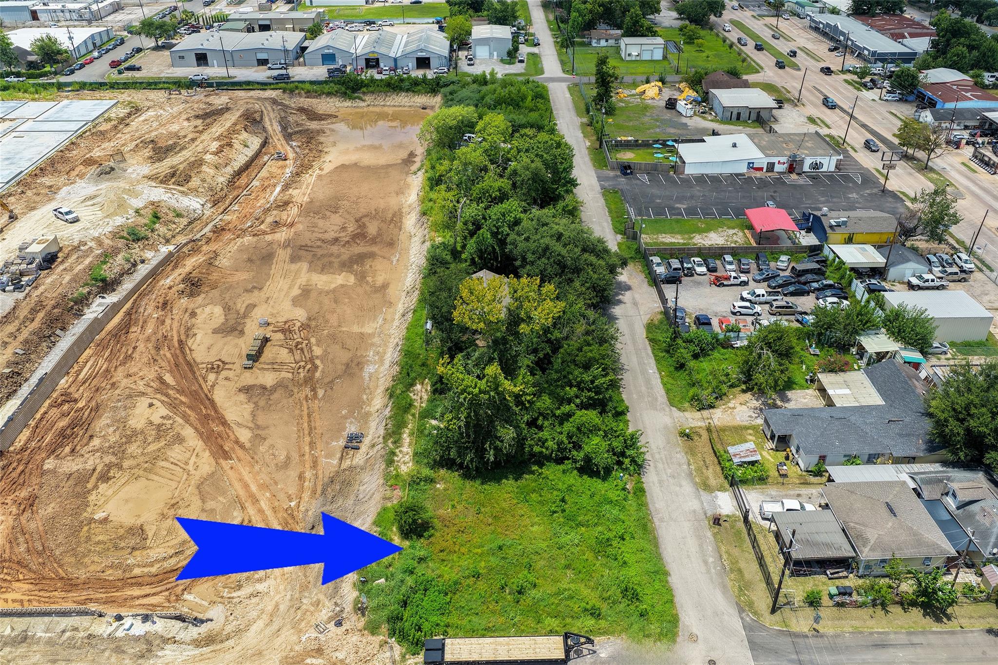 Aerial view of a vacant grassy lot beside a cleared construction site and neighborhood road.