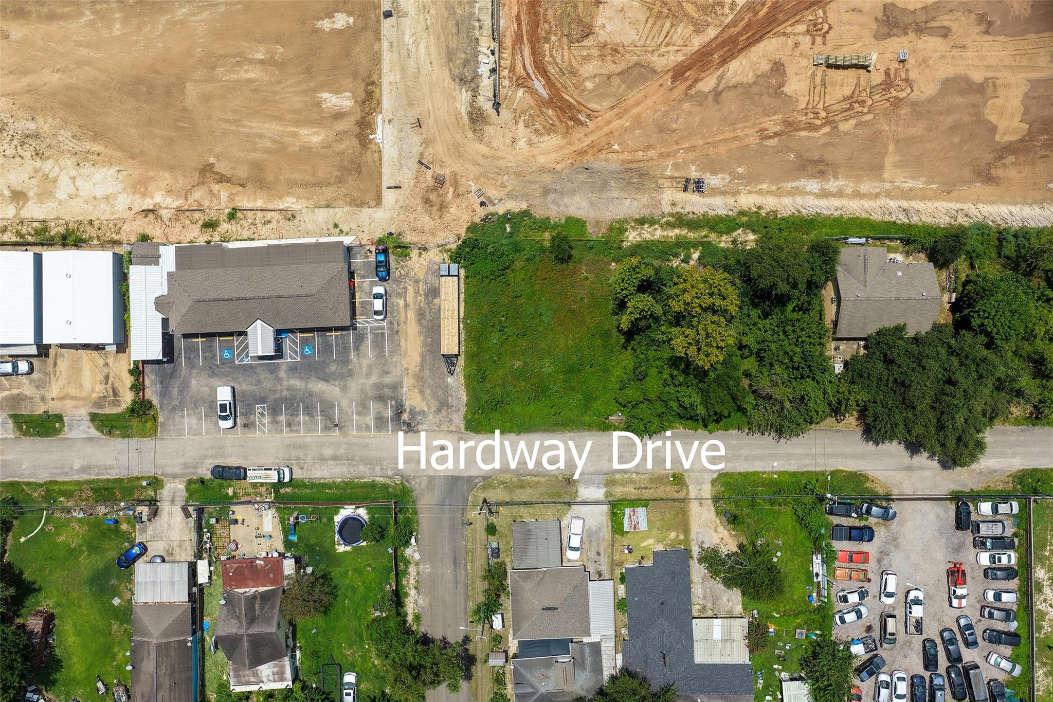 Aerial view of a vacant green lot beside Hardway Drive, with trees and nearby buildings.