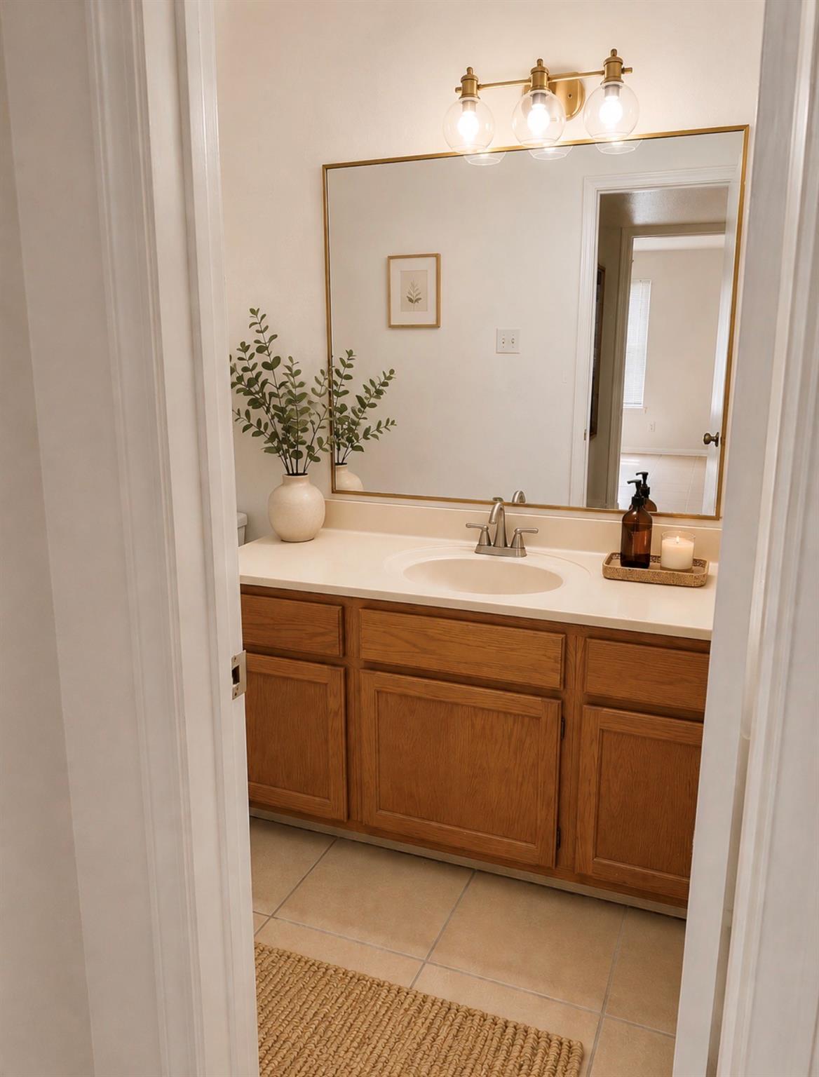 Bathroom vanity with warm wood cabinets, a gold-framed mirror, and three globe lights.