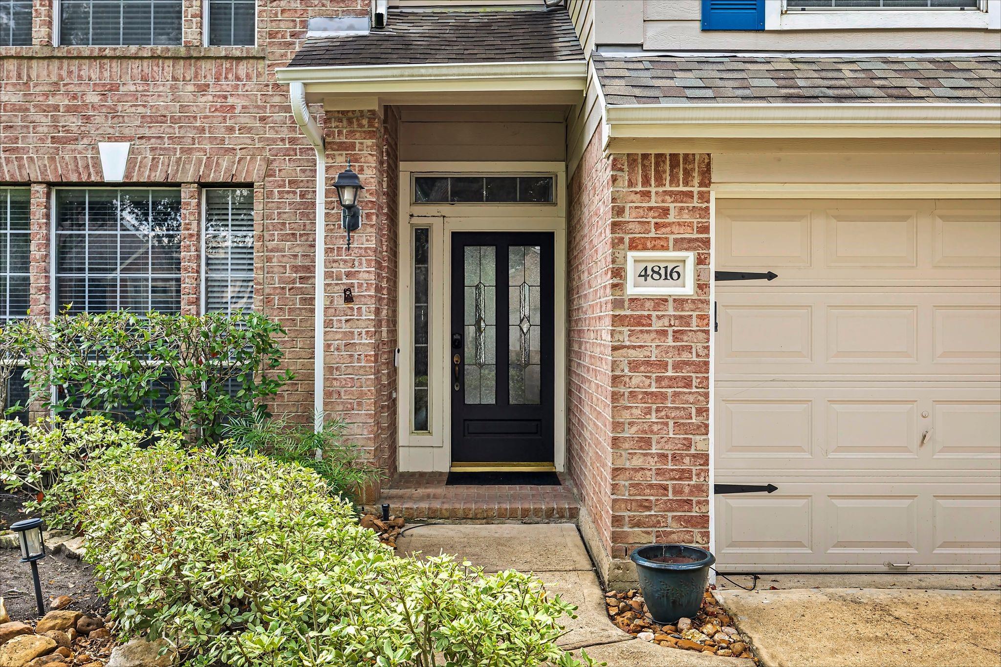 Brick home entrance with a black glass-paneled door, cream garage, and address number 4816.