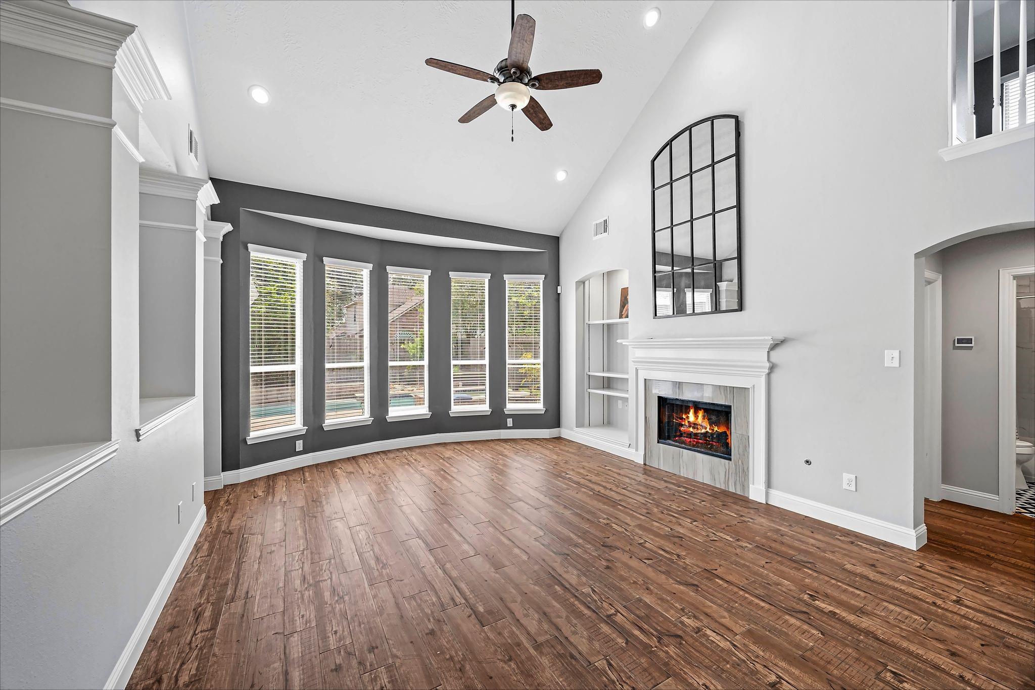 Vacant living room with a vaulted ceiling, wood floors, tall windows, and a fireplace.