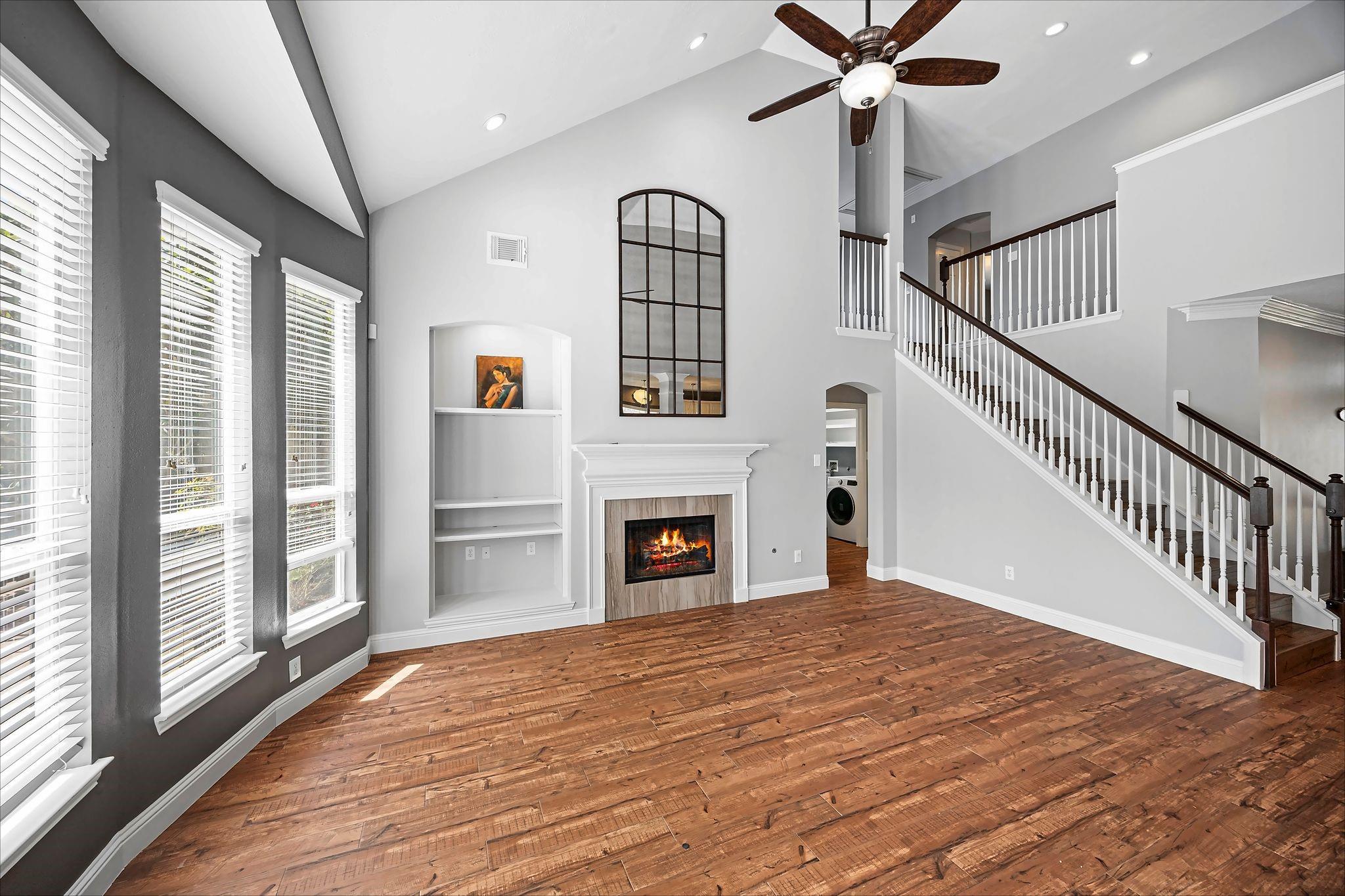 Vacant living room with a fireplace, vaulted ceiling, wood floors, and a staircase.
