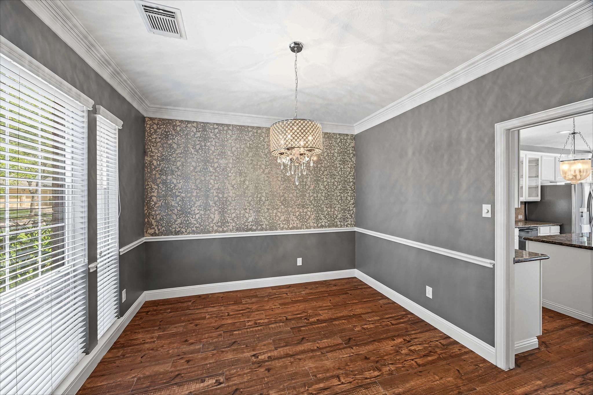 Empty dining room with a crystal chandelier, patterned accent wall, and dark wood flooring.