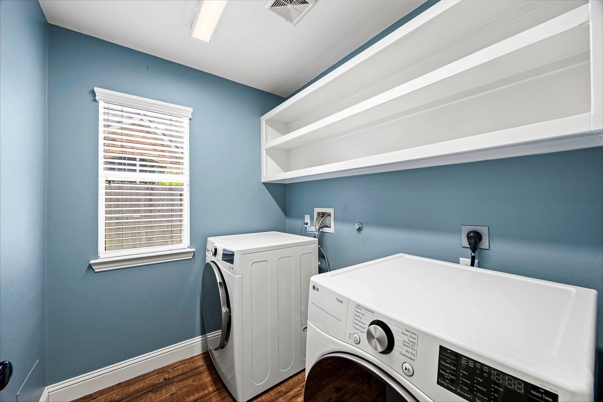 Laundry room with white washer and dryer, built-in shelving, and a window with blinds.