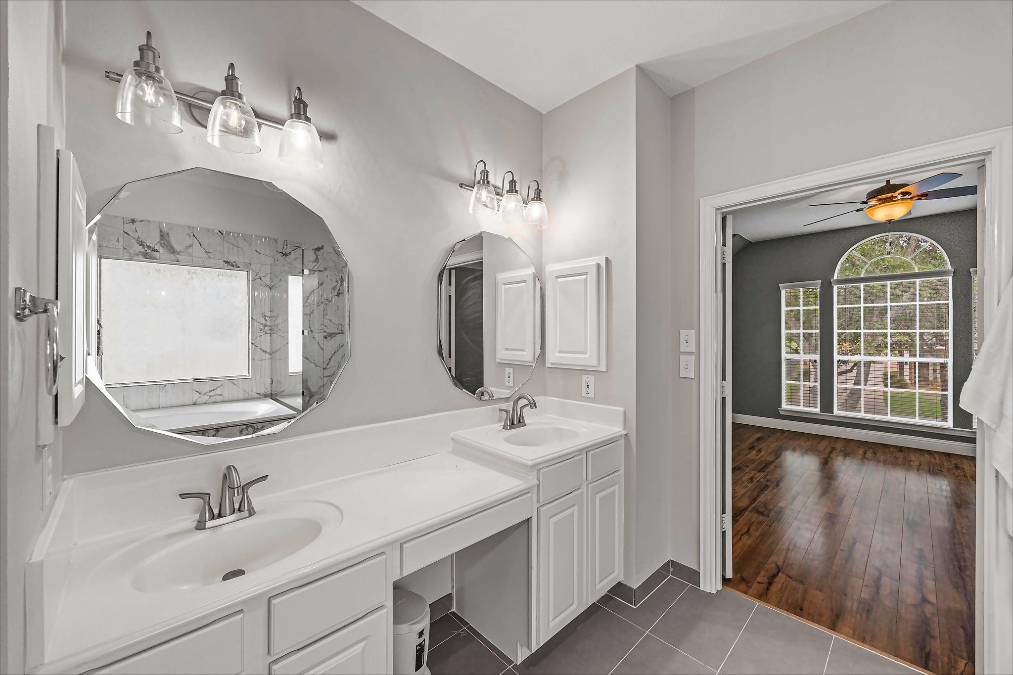 Bathroom with a white double vanity and octagonal mirrors, opening to a room with an arched window.