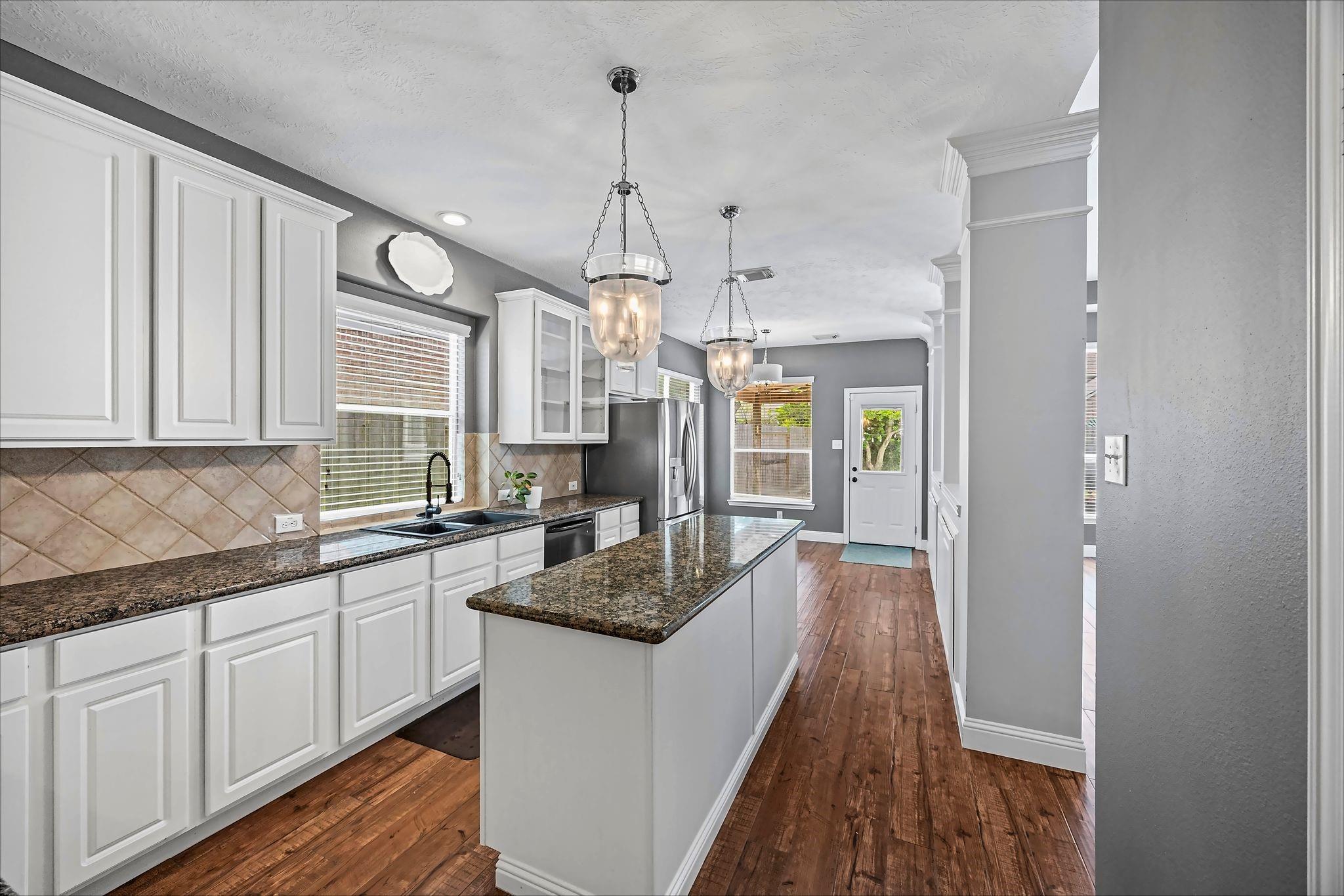 Kitchen with a granite-topped island, white cabinets, stainless appliances, and warm wood floors.