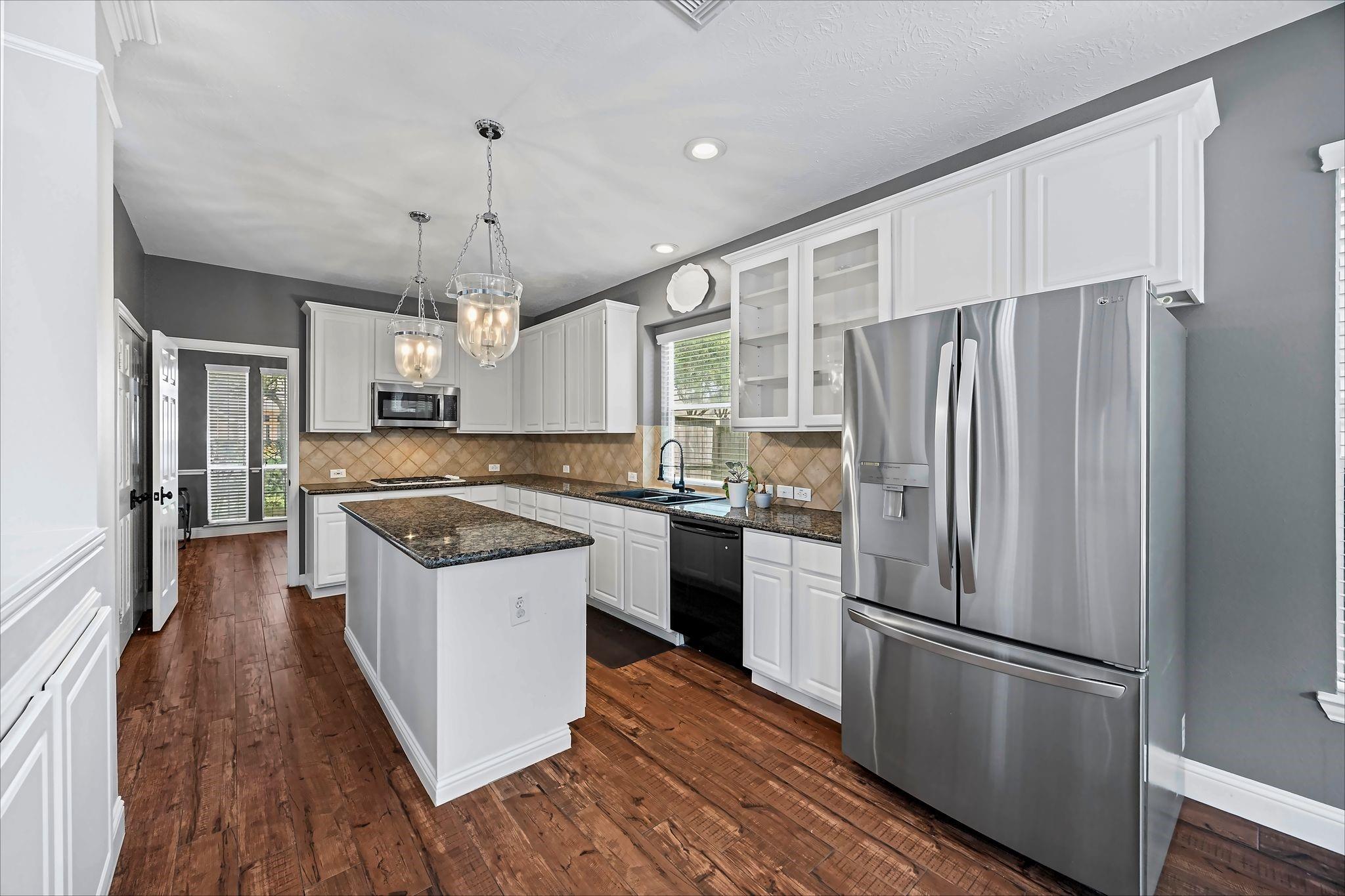 Kitchen with a central island, white cabinetry, stainless steel appliances, and warm wood flooring.