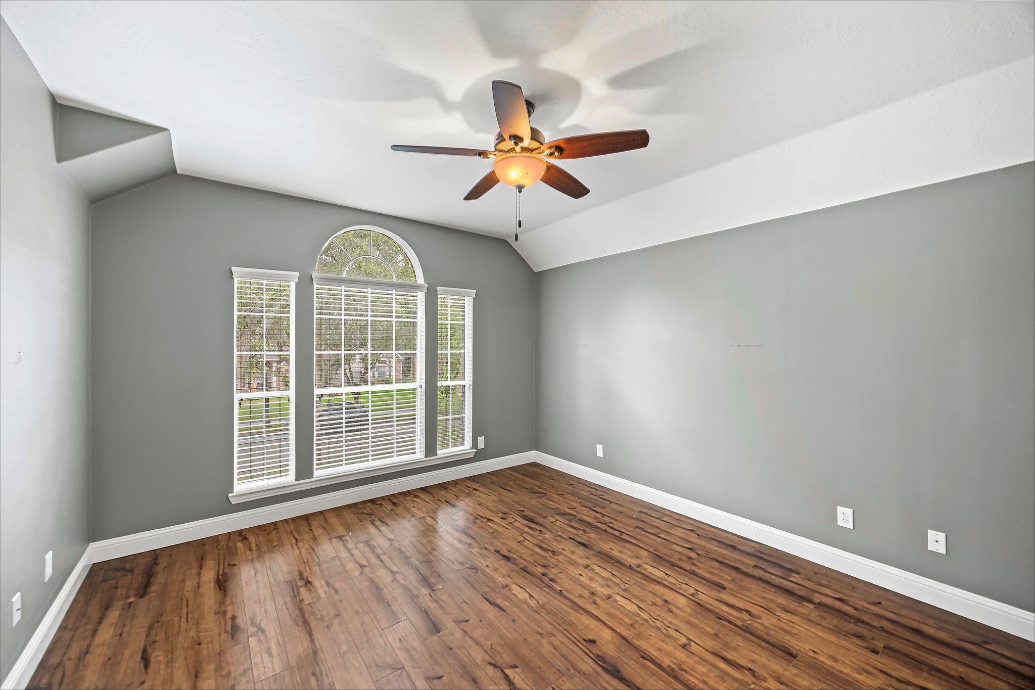 Empty room with hardwood floors, vaulted ceiling, and a large arched window with white blinds.