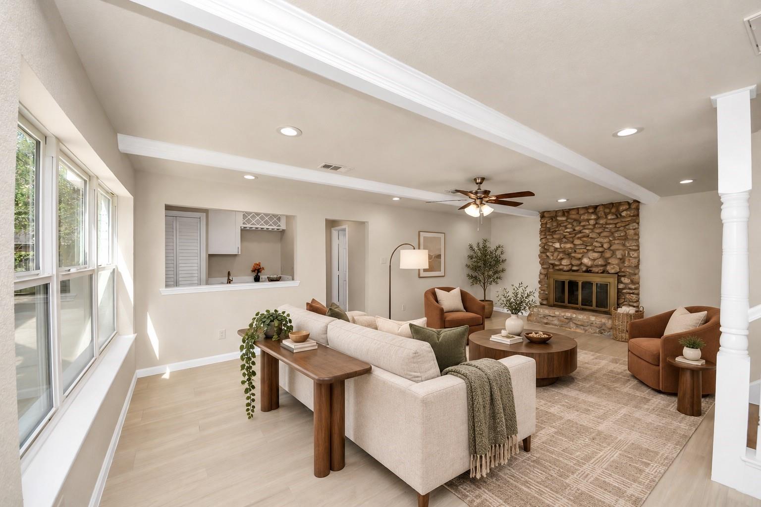 Living room with a stone fireplace, pale sofas, rust-colored armchairs, and broad windows.