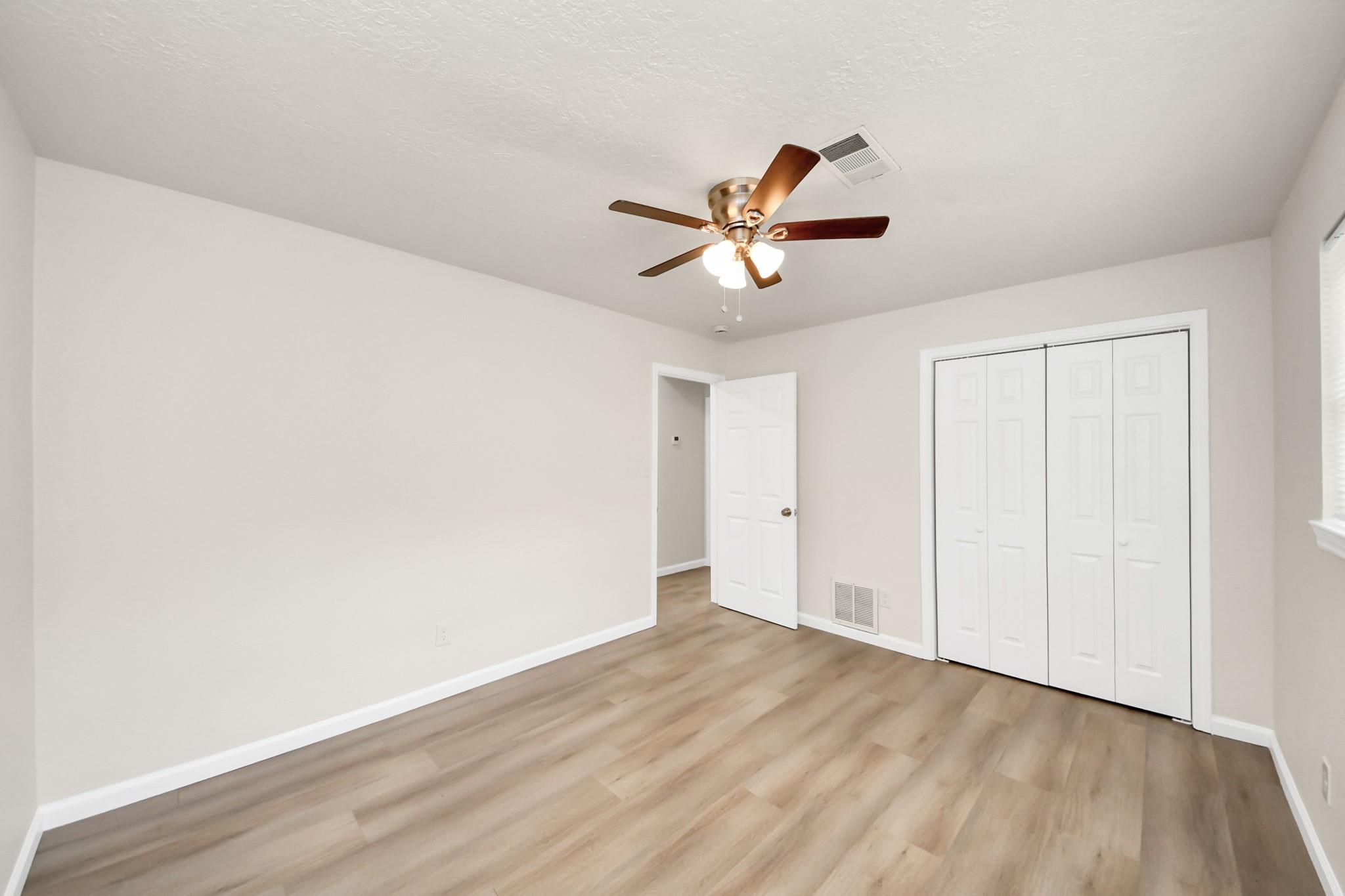 Vacant bedroom with light wood-look flooring, a ceiling fan, and white folding closet doors.