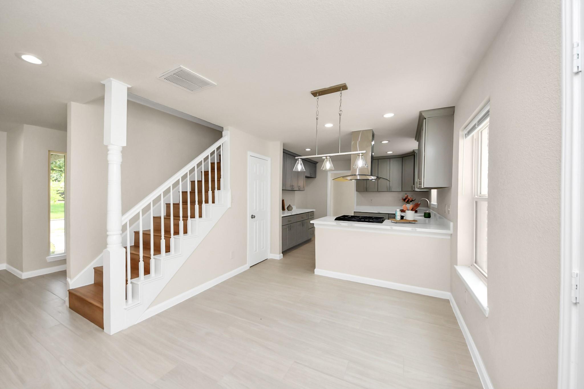 Open kitchen and dining area with gray cabinets, pendant lights, and a white-railed staircase.