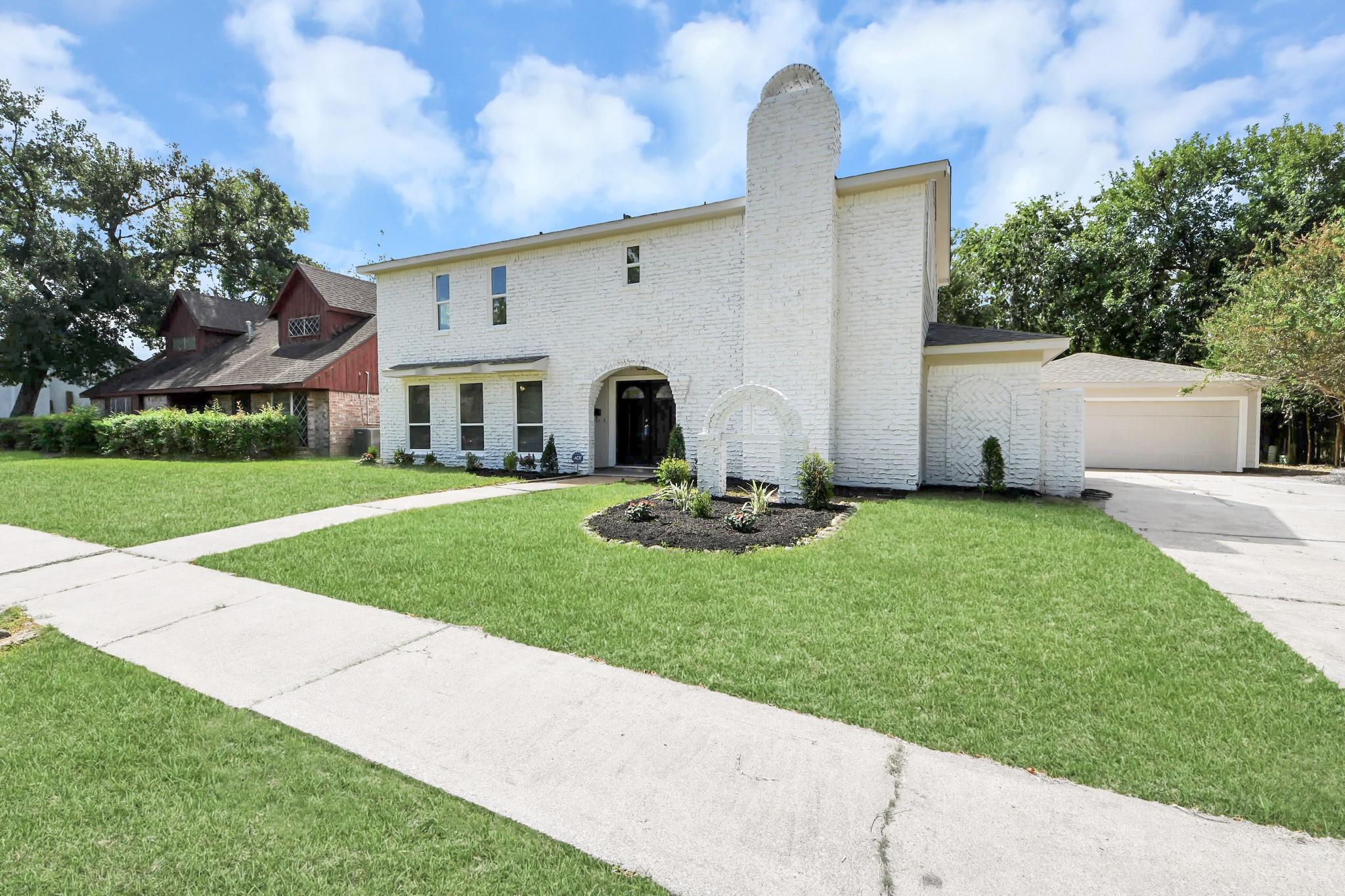 Two-story white brick house with a tall chimney and arched entry, front lawn and attached garage.