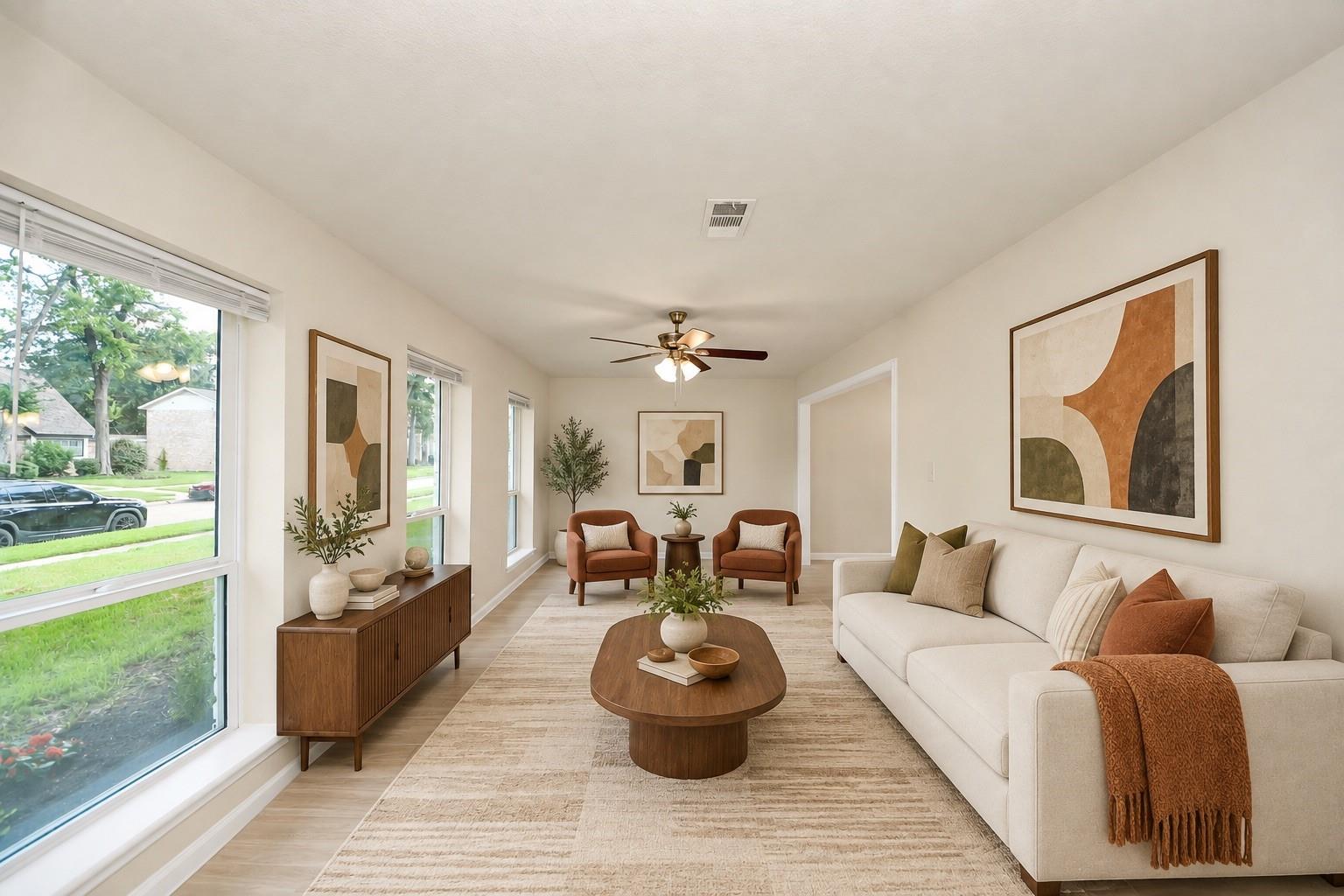Staged living room with a white sofa, rust-colored armchairs, and large street-facing windows.