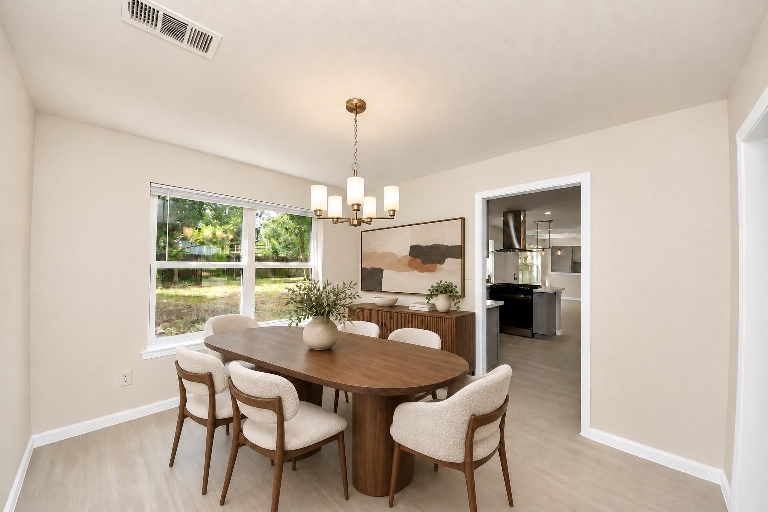 Dining room with an oval wooden table, upholstered chairs, and a large window overlooking greenery.