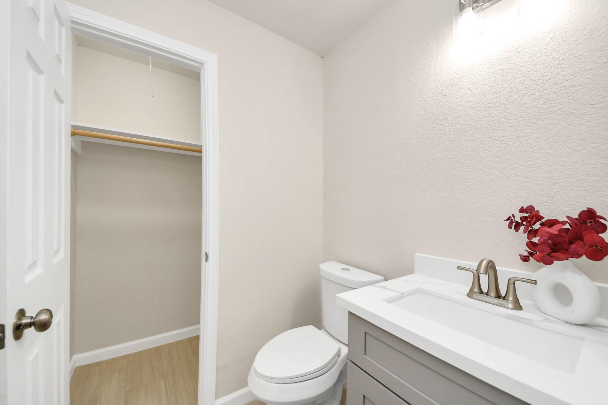 Bright bathroom with a white vanity and toilet beside an open closet.