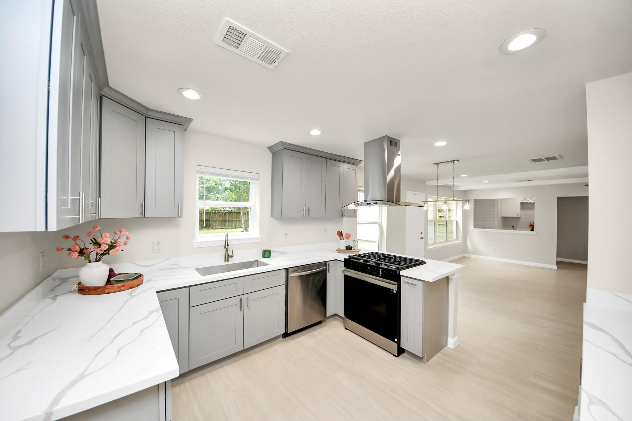 Kitchen with gray shaker cabinets, marble-look counters, and a stainless steel gas range.