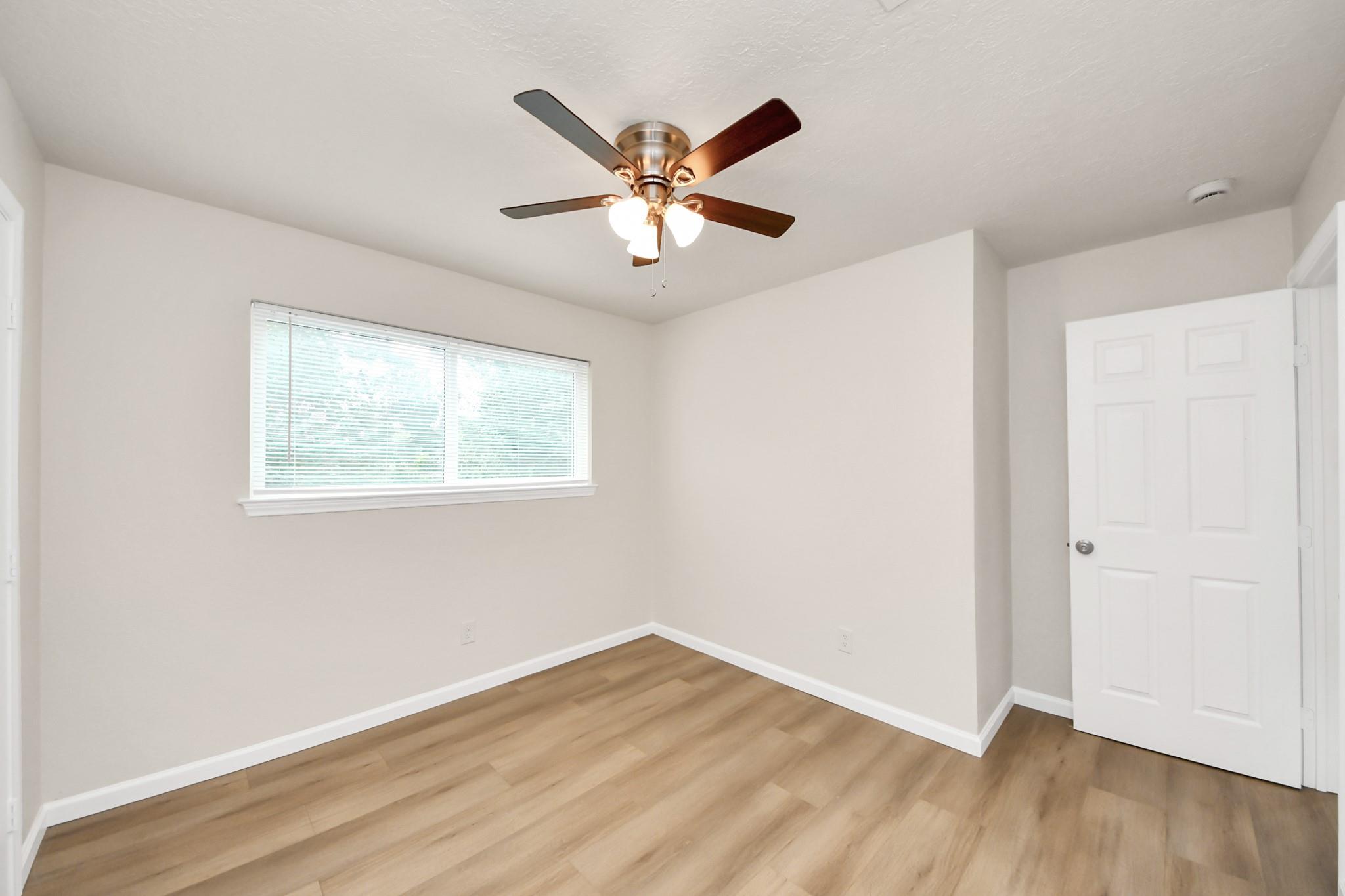 Empty bedroom with wood-look flooring, window blinds, and a ceiling fan with lights.