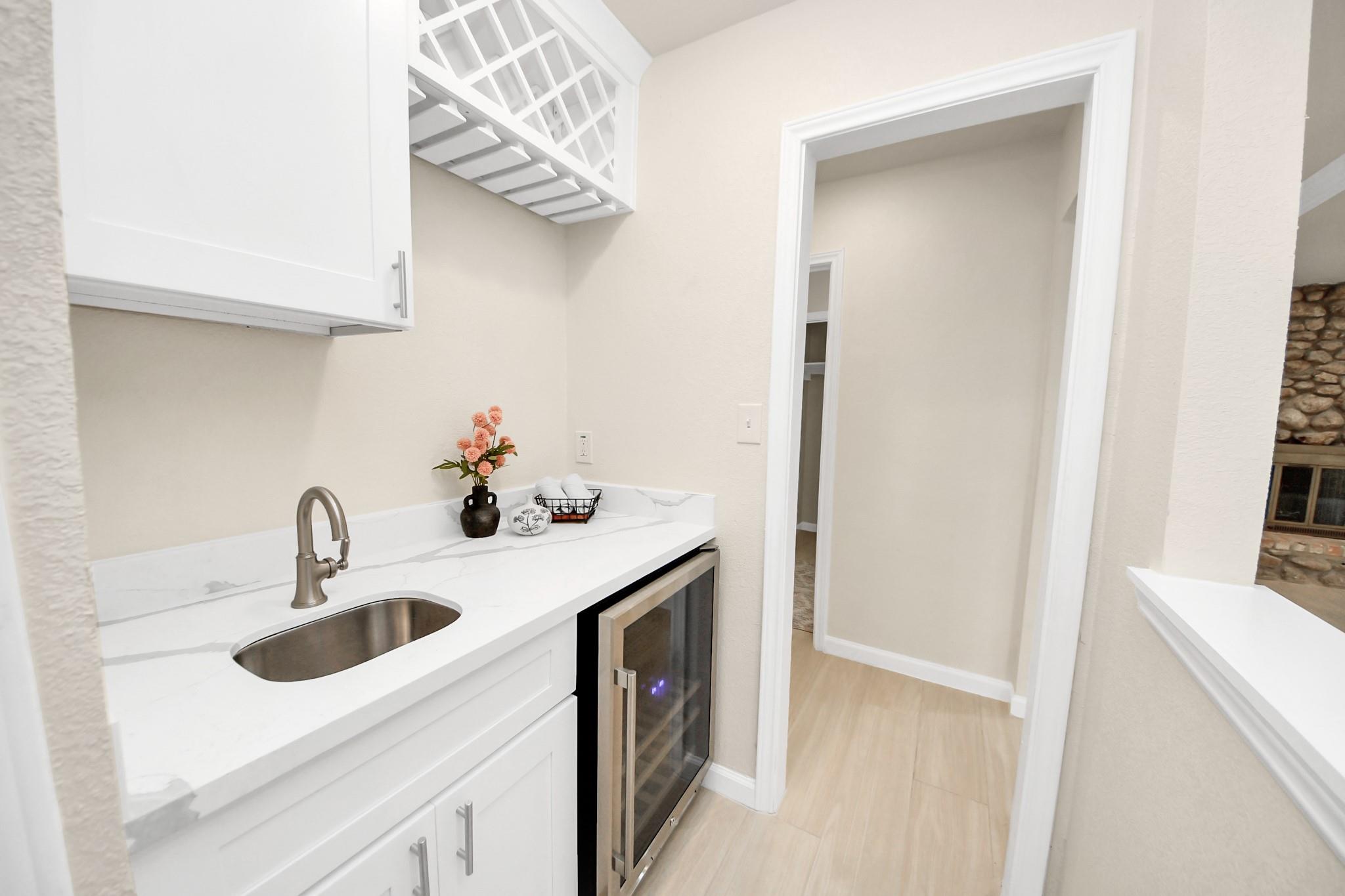 Wet bar with white cabinets, a marble-look counter, undermount sink, and beverage refrigerator.