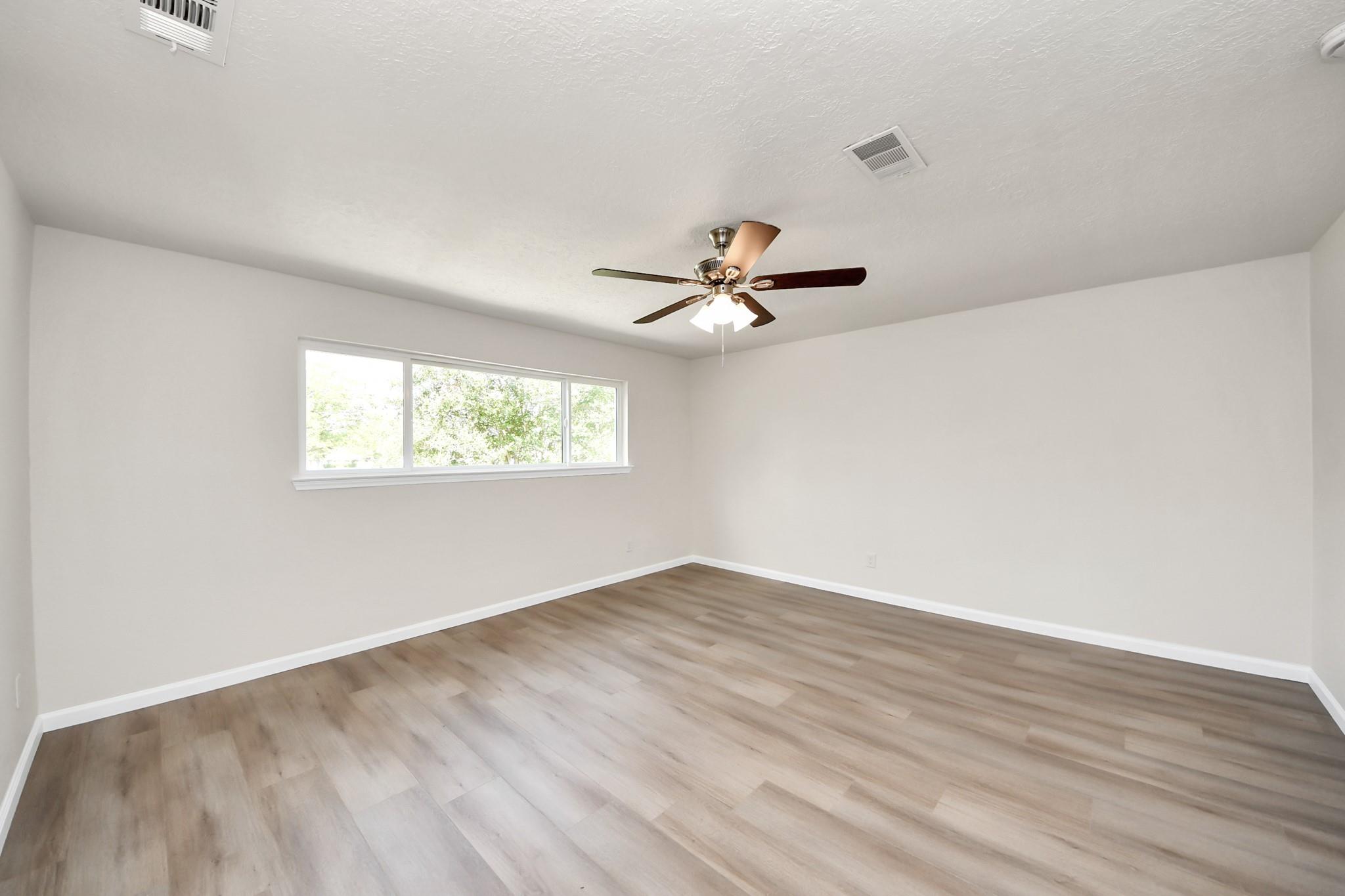 Empty room with wood-look flooring, a wide window, and a ceiling fan with lights.