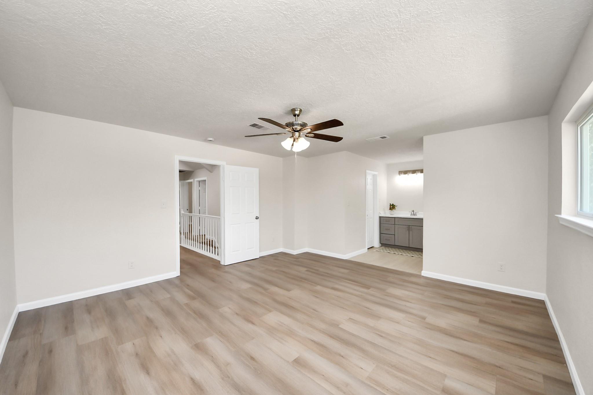 Vacant bedroom with wood-look floors, ceiling fan, and an open view to the bathroom vanity.